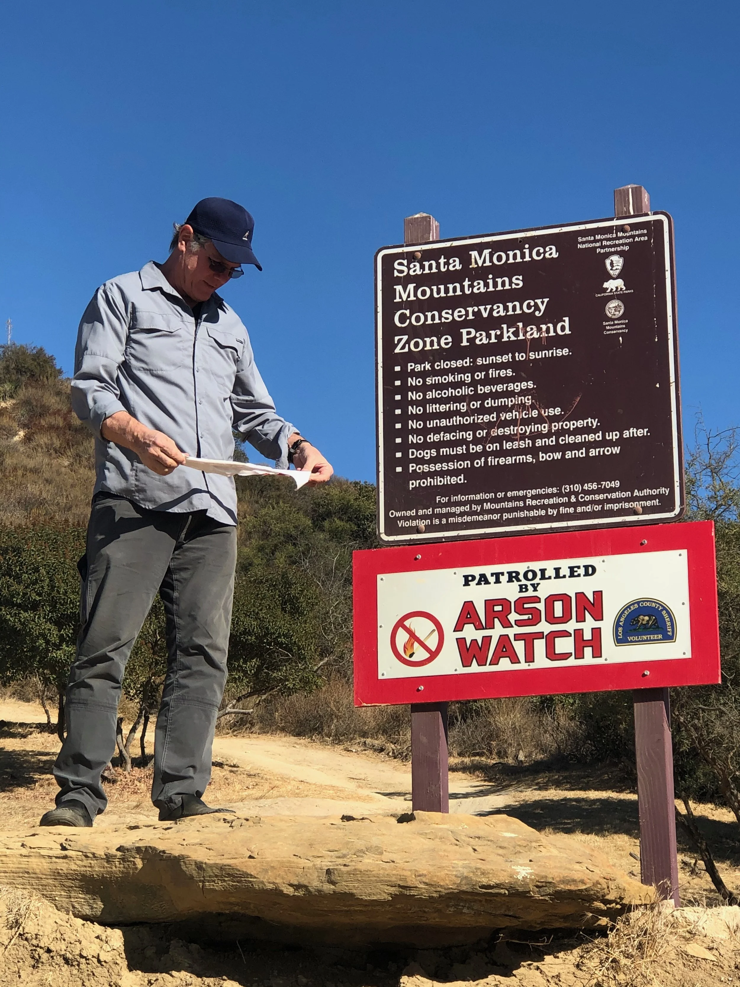 Arson Watch volunteer standing next to a 'Santa Monica Mountains Conservancy Zone Parkland' and 'Patrolled by Arson Watch.