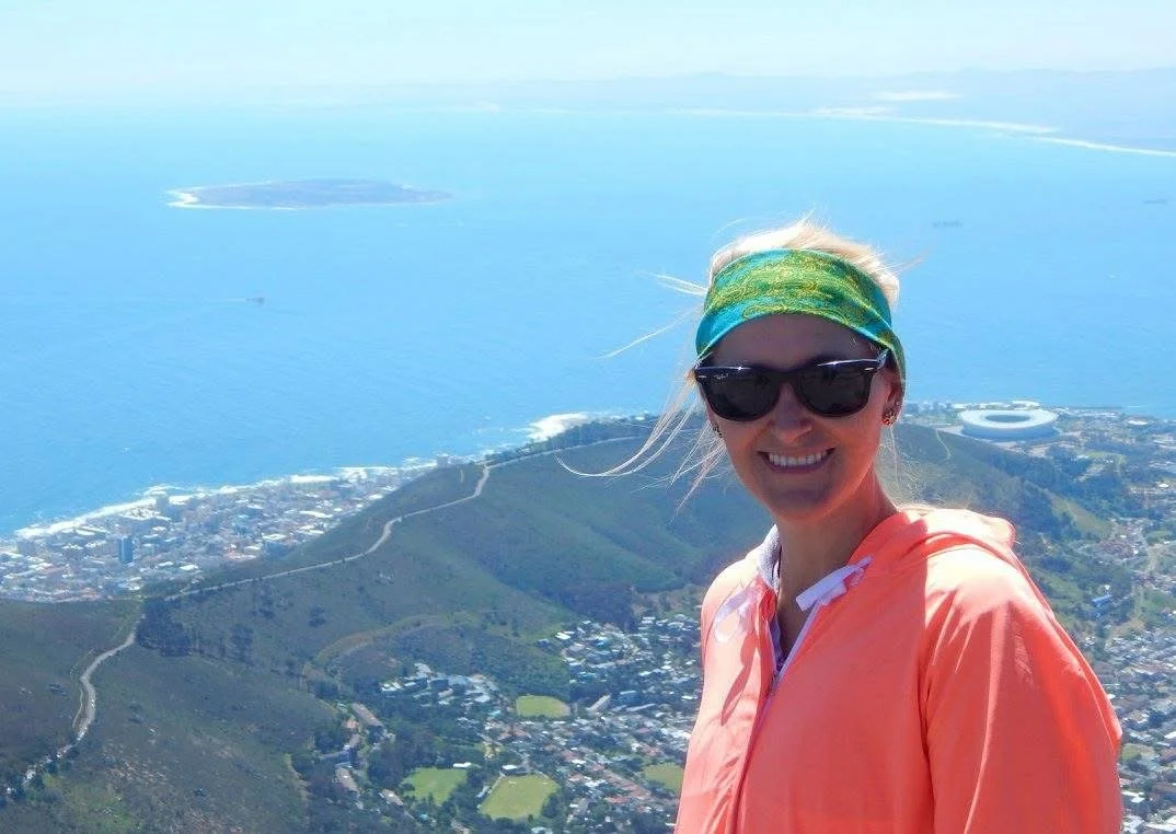 A woman taking a selfie atop Table Mountain, with Cape Town and the ocean behind her.