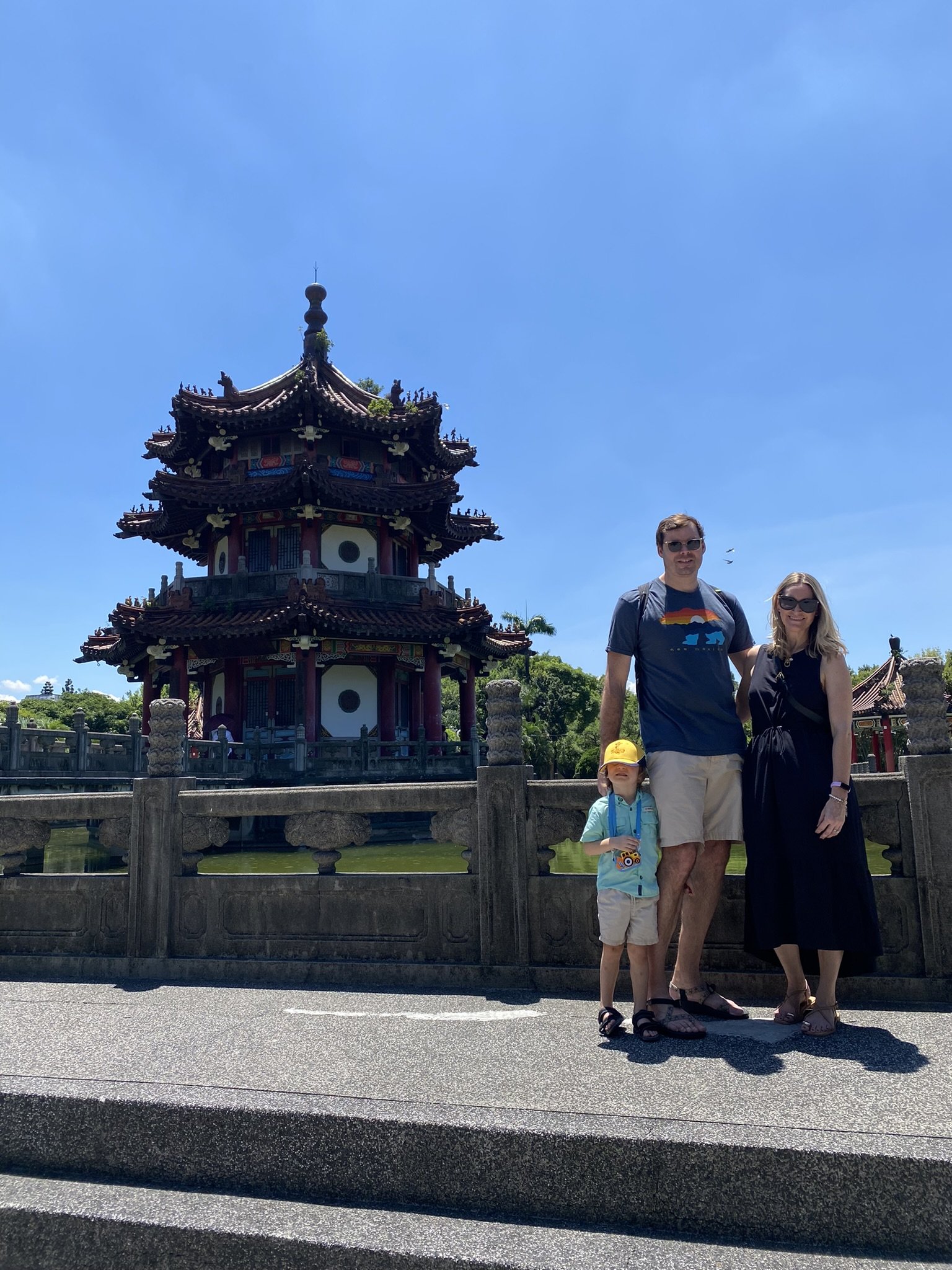 Two adults and a child standing beside an ornate pavilion in Taipei.