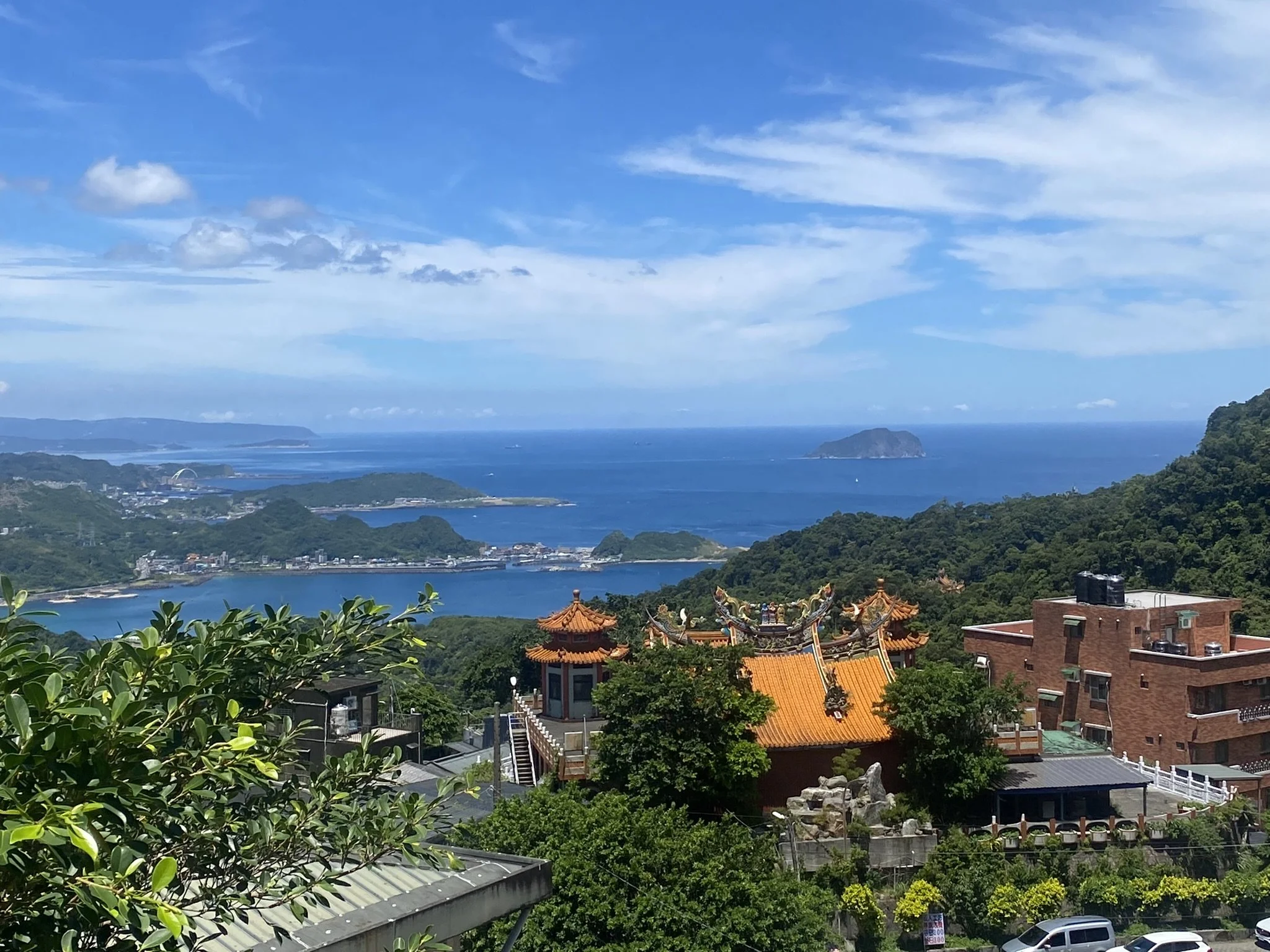 Orange-roofed buildings in Jiufen overlooking green hills and the sea.