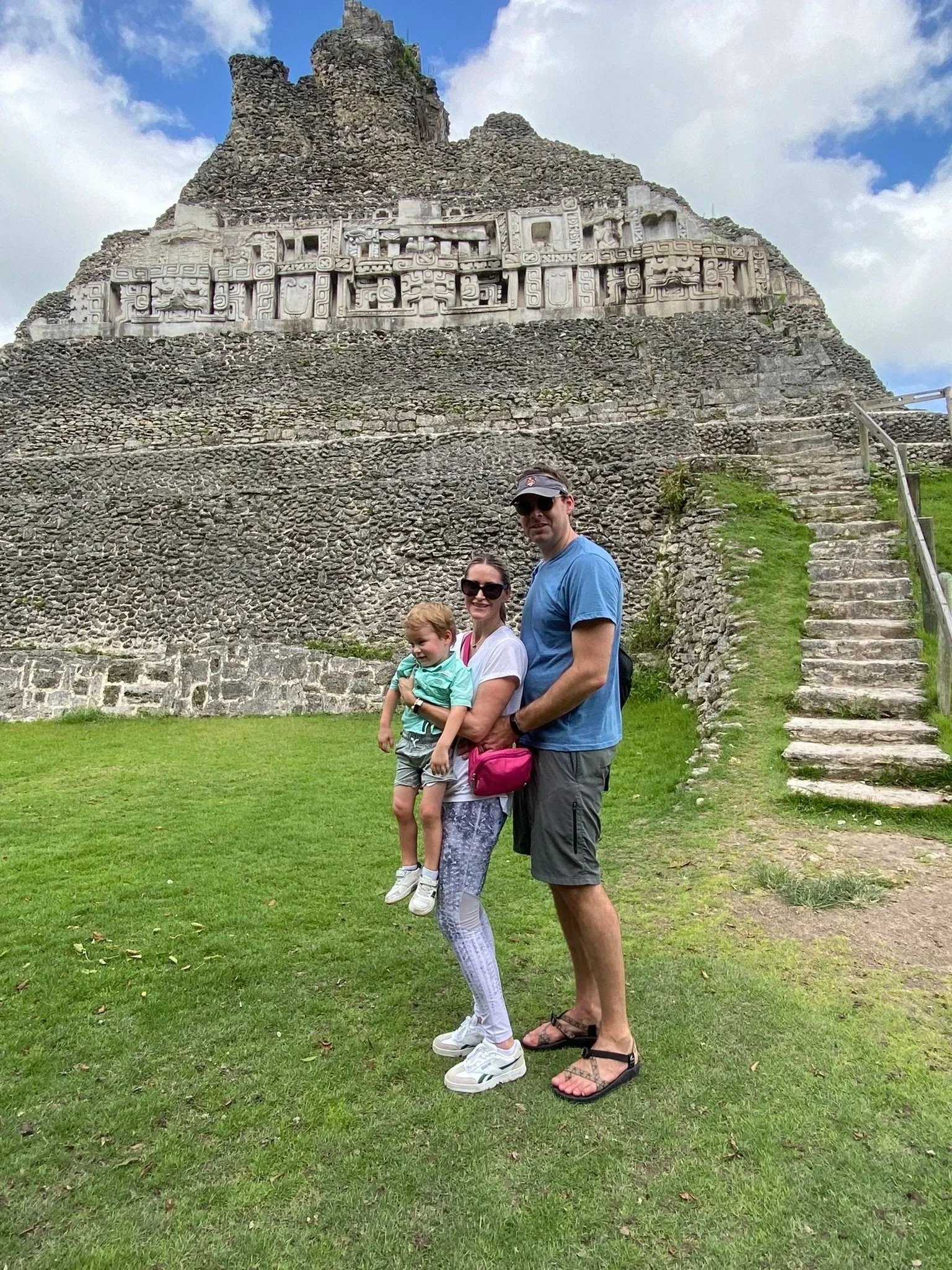 Family of three standing in front of the stone pyramid at Xunantunich in Belize.