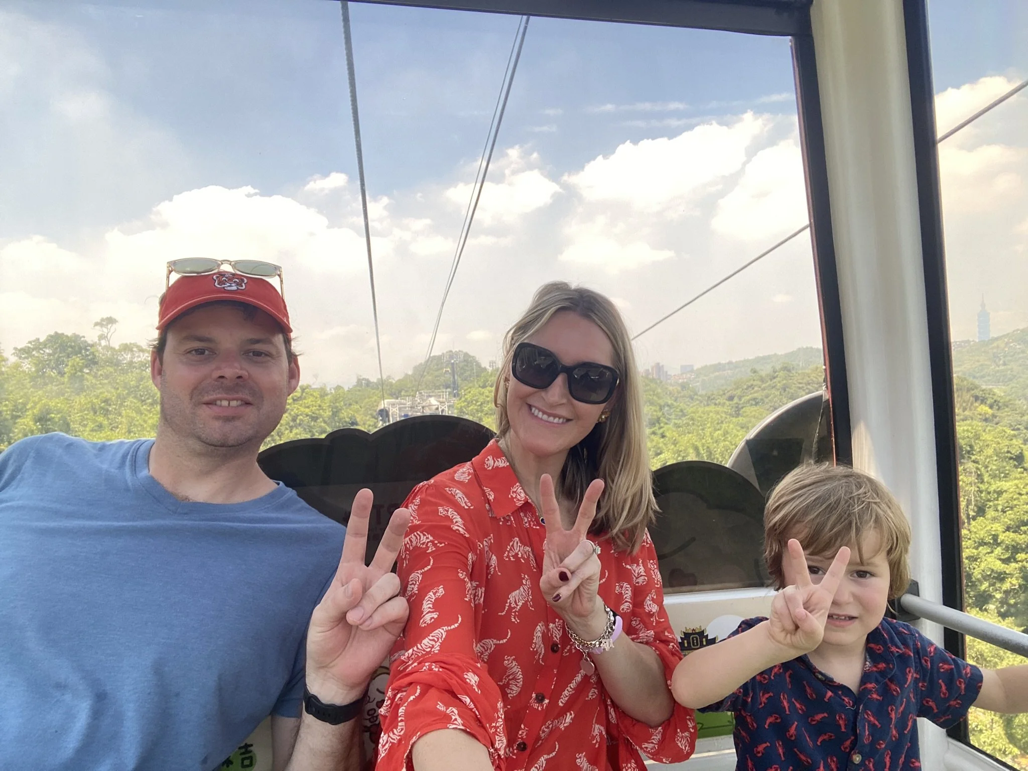 Two adults and a child smiling inside a Maokong Gondola cabin, with green hills behind them.