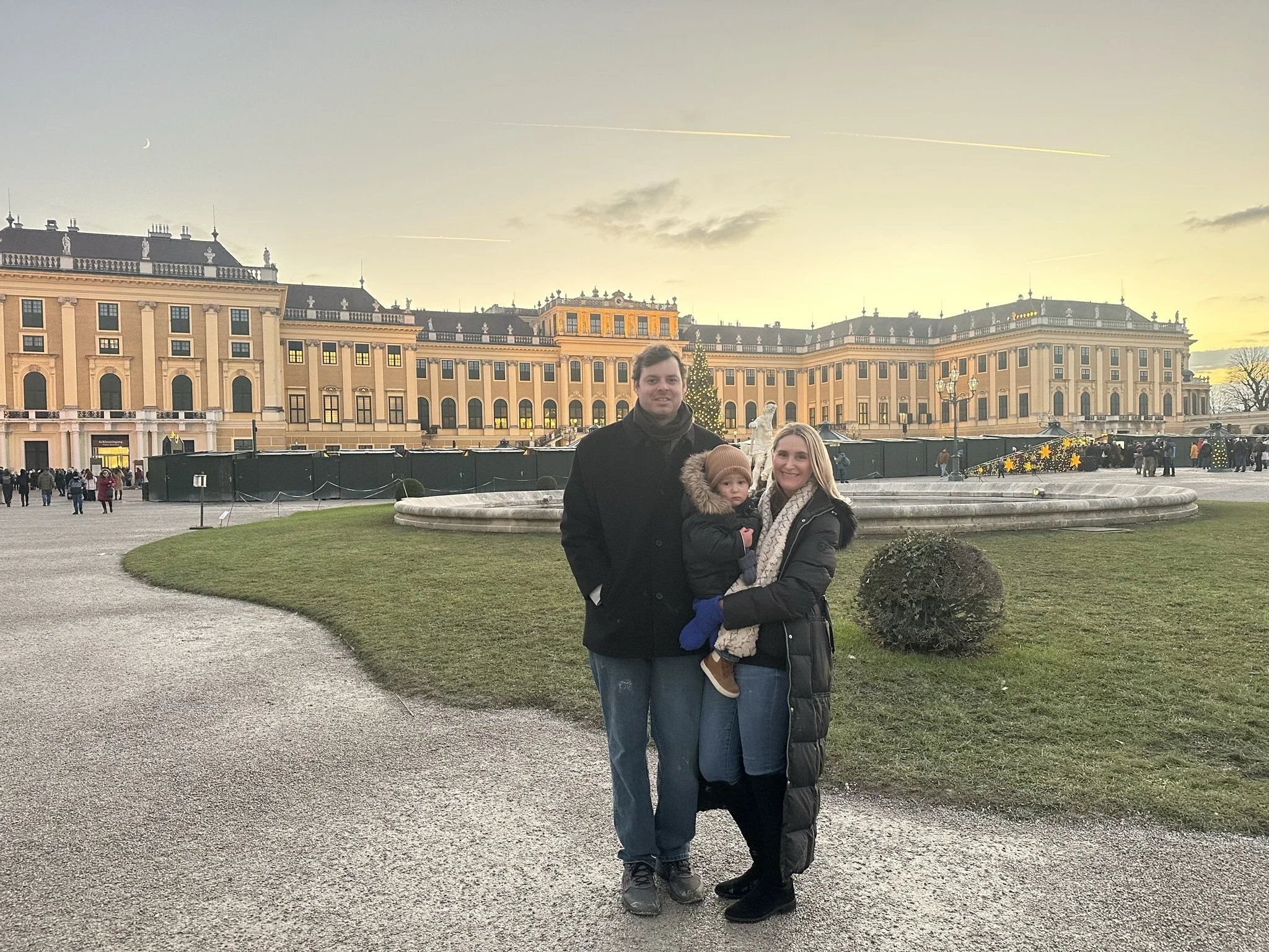 A family of three in front of Schönbrunn Palace in Vienna at sunset.
