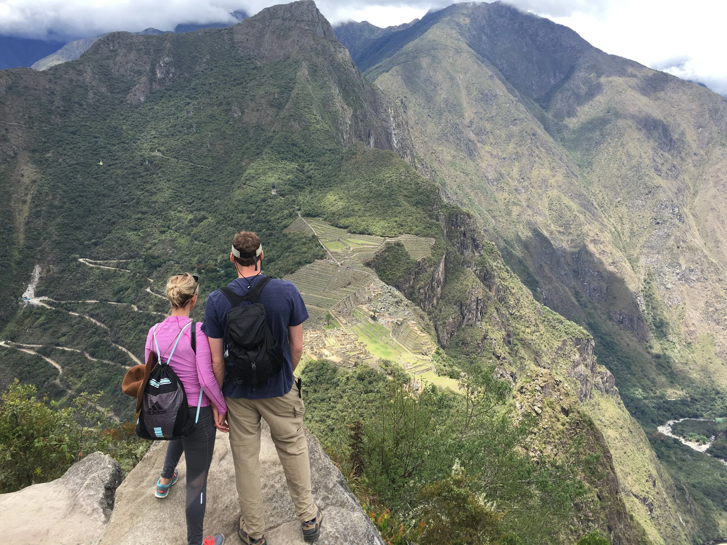 Two hikers on Huayna Picchu overlooking Machu Picchu and the surrounding mountains in Peru.
