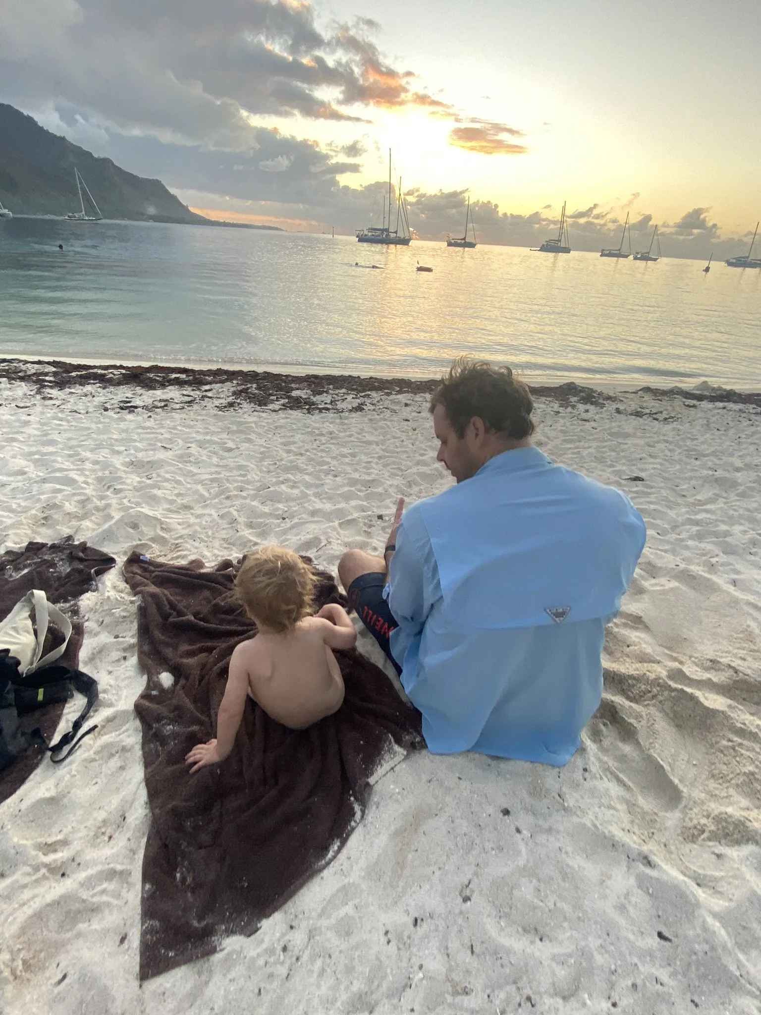 Father and young son sitting on the sand at Ta’ahiamanu Beach in Moorea at sunset.