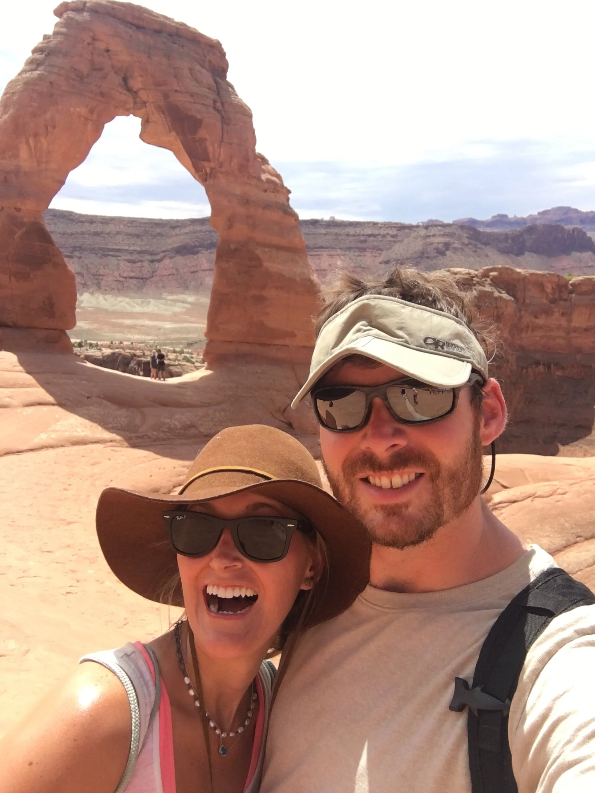 Couple taking a selfie with Delicate Arch behind them in Arches National Park, Utah.