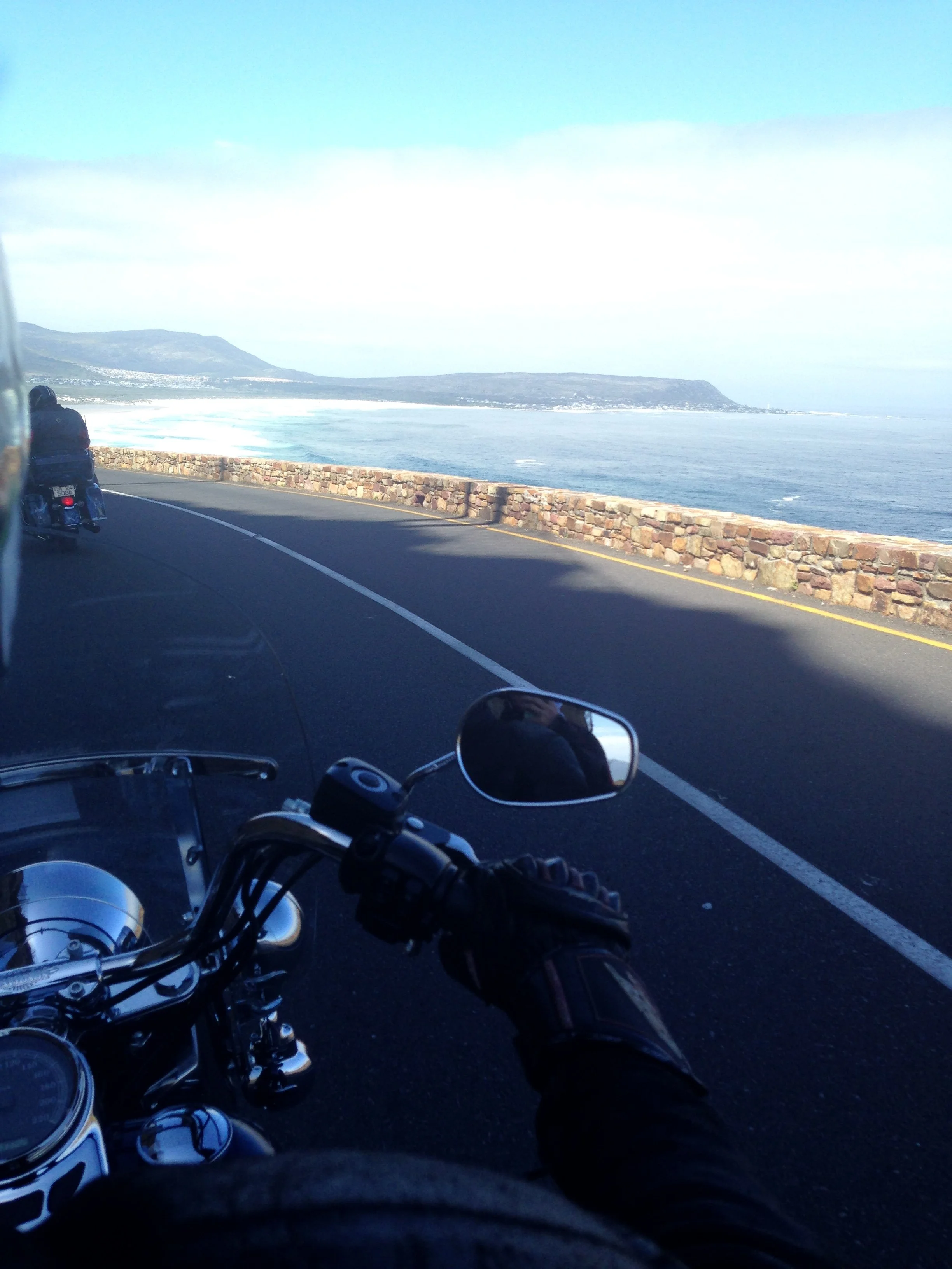 View from a motorcycle on a coastal road toward the Cape of Good Hope.