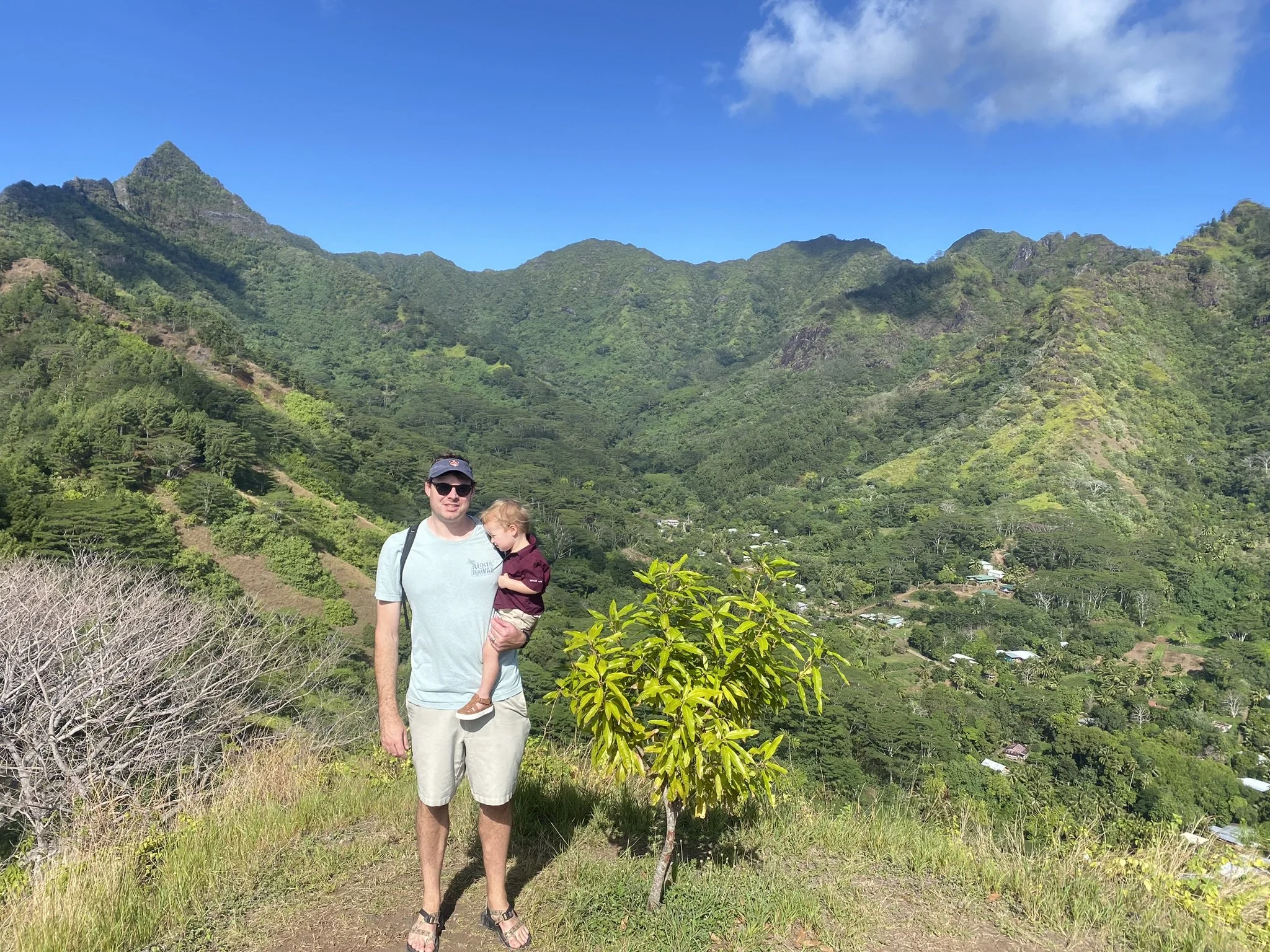 Father holding his young son at a viewpoint overlooking the green mountains of Moorea, French Polynesia.