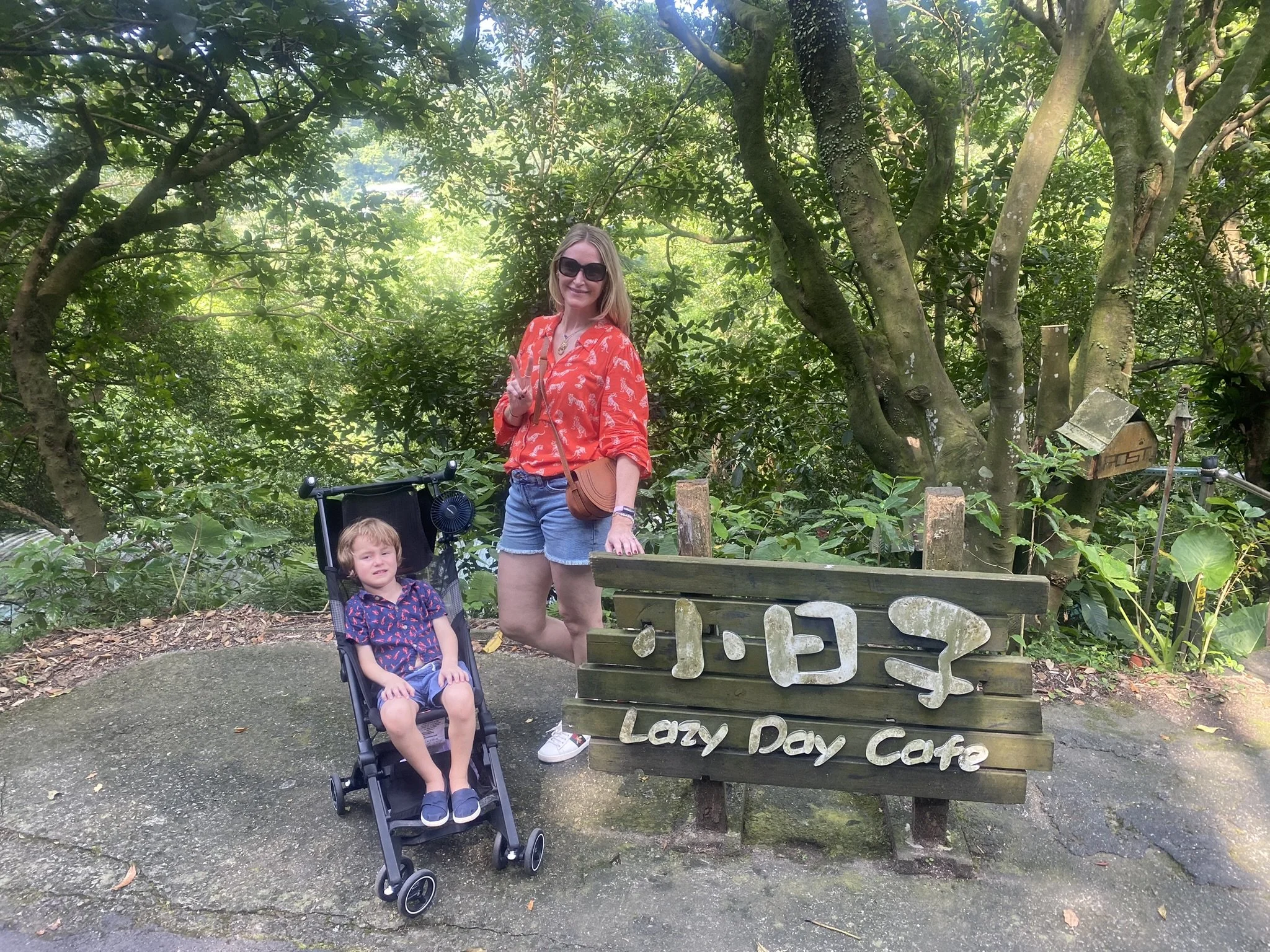 An adult and a child beside the Lazy Day Cafe sign among the trees in Jiufen.