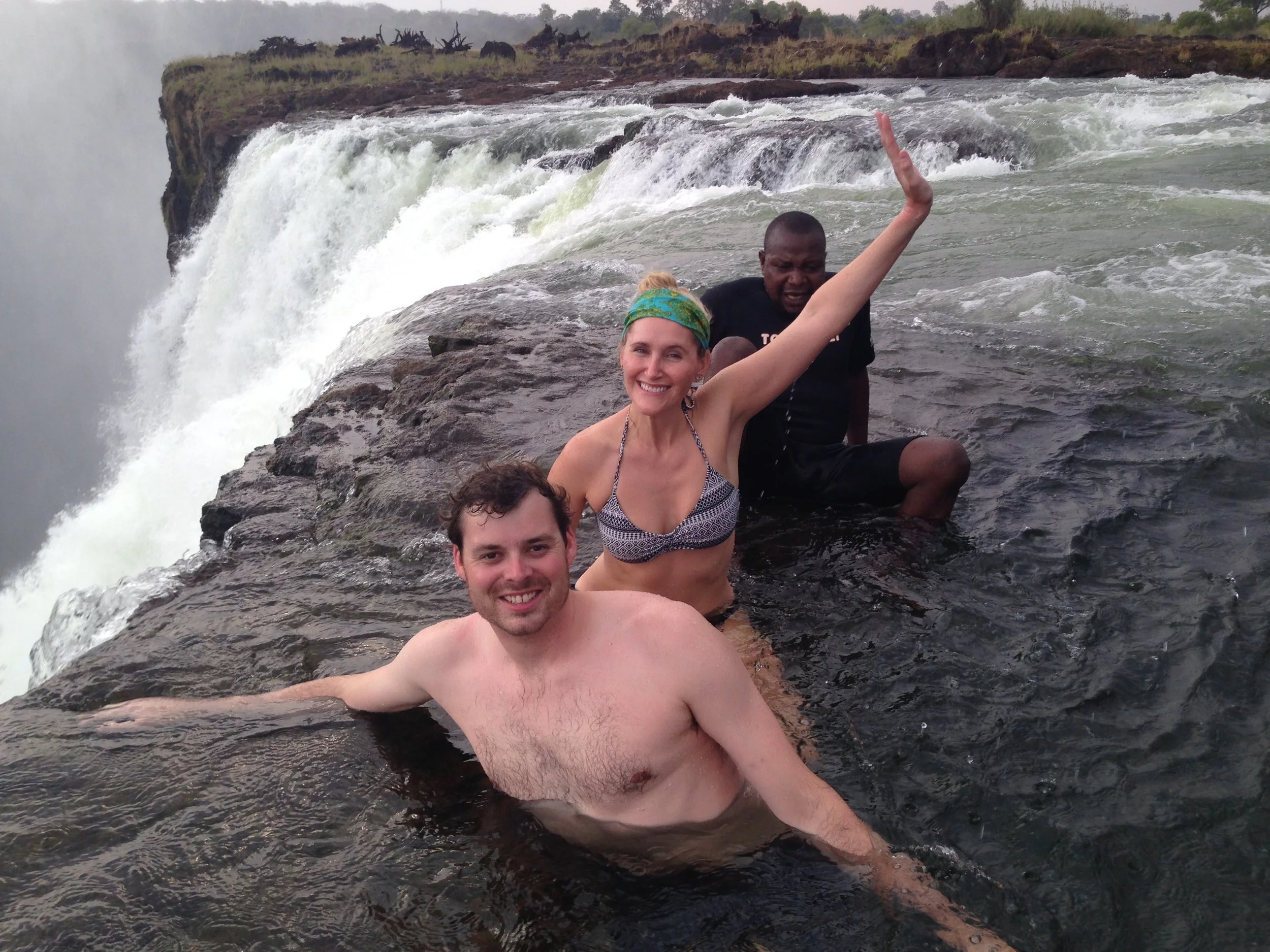 Three people in the water at Devil’s Pool, beside the edge of Victoria Falls.