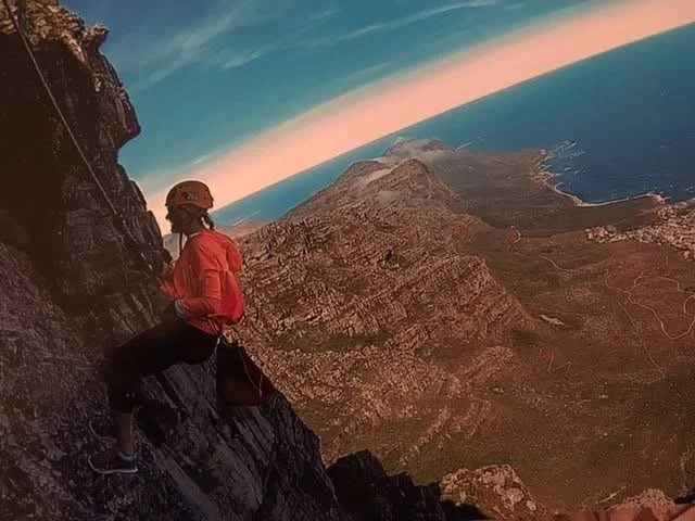 A person abseiling down Table Mountain above the Cape Town coastline.