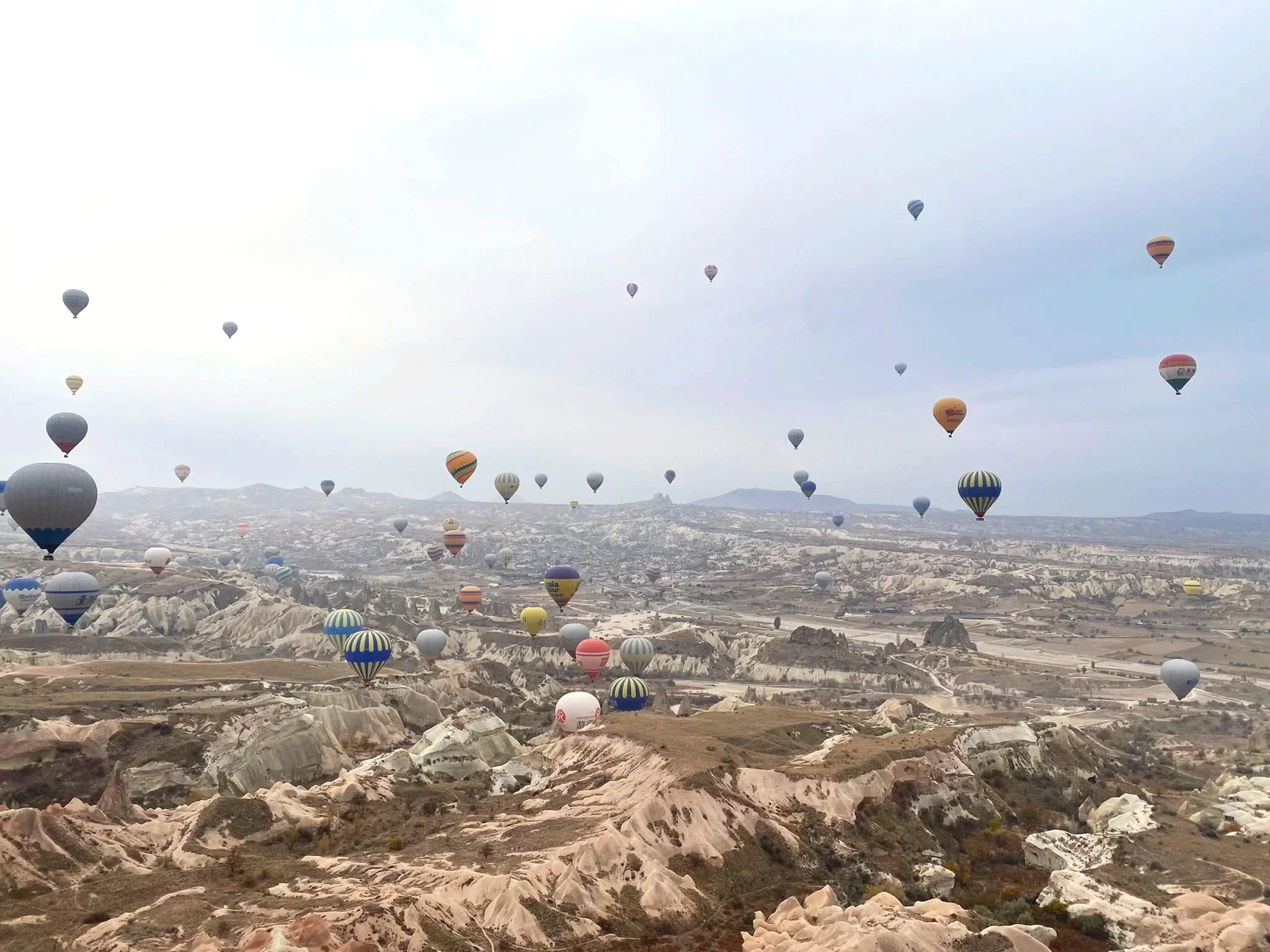 Hot air balloons floating over Cappadocia’s rocky landscape, viewed from another balloon.