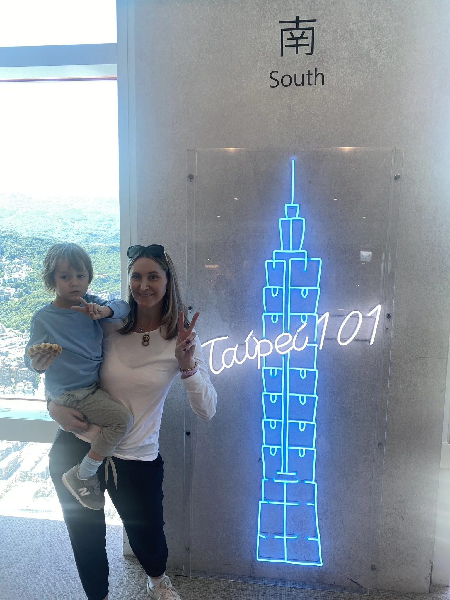 A woman holding a child beside a glowing Taipei 101 display inside the tower.