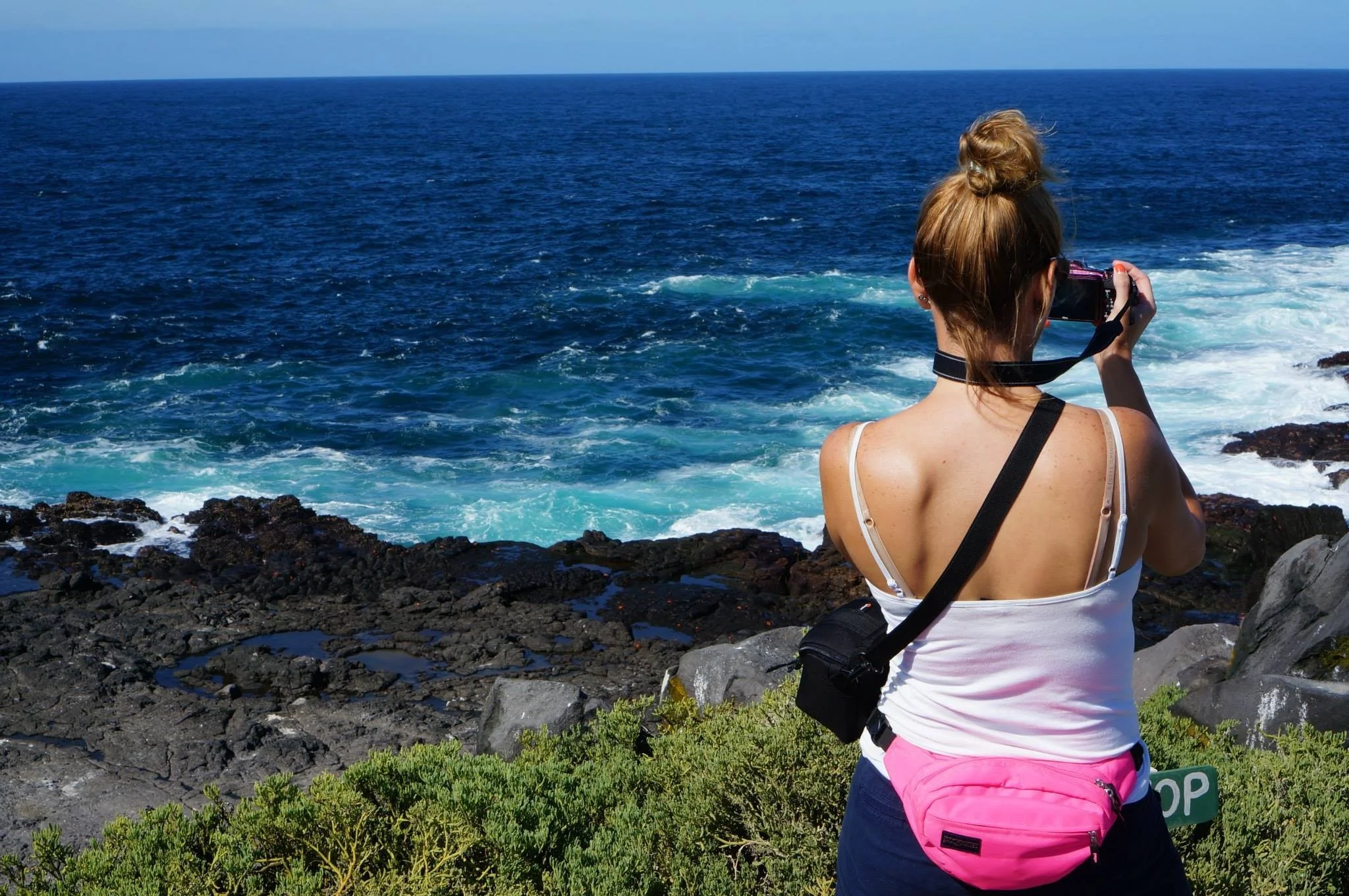 Woman photographing the ocean from a rocky coastline in the Galápagos Islands.