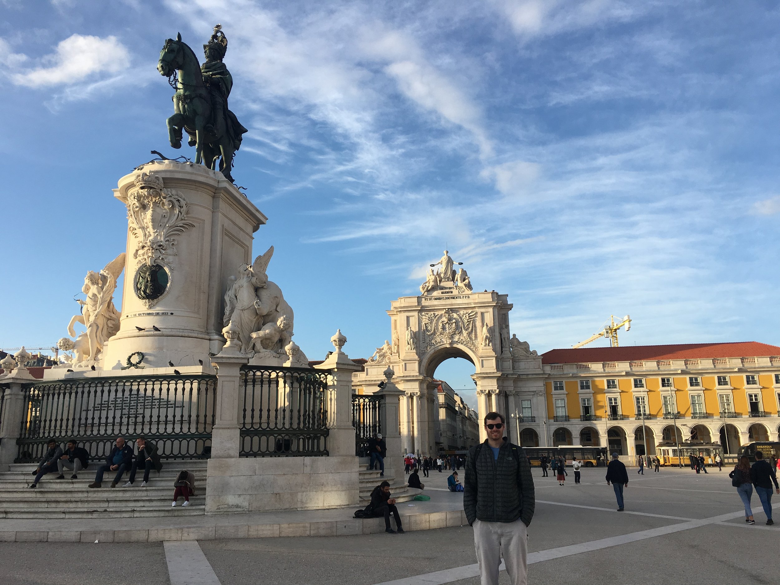 A man standing in Lisbon’s Praça do Comércio, with its equestrian statue and triumphal arch behind him.