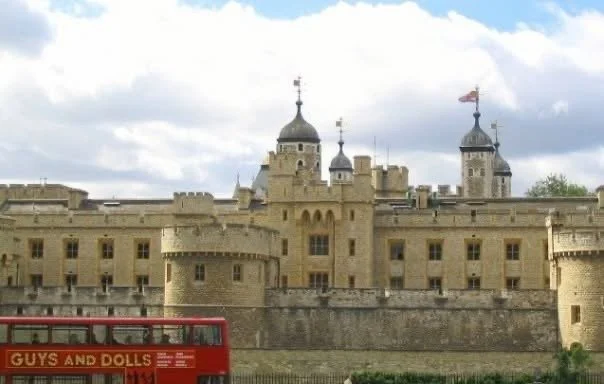 The Tower of London behind its stone walls, with a red bus passing in front.