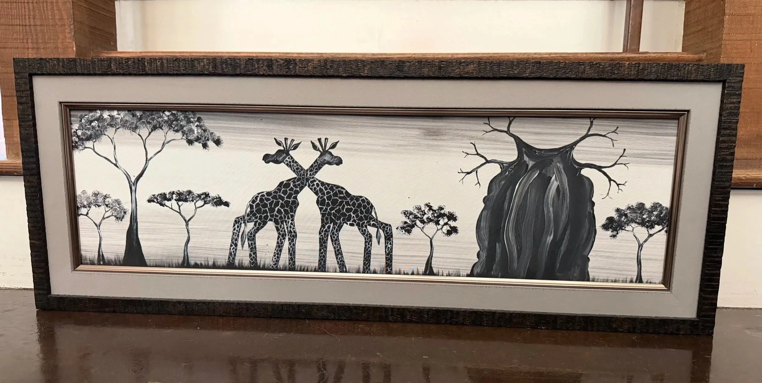 Framed black-and-white artwork of giraffes beneath trees, brought home from South Africa.