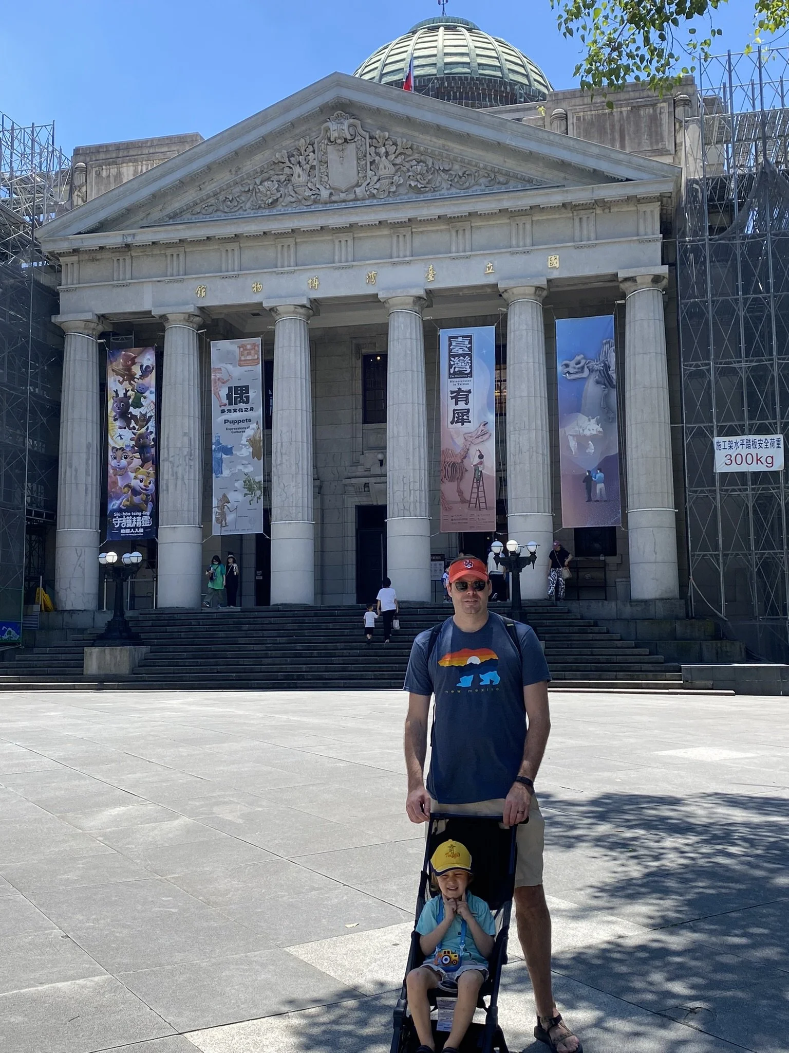An adult and a child in a stroller outside the columned entrance of the National Taiwan Museum.