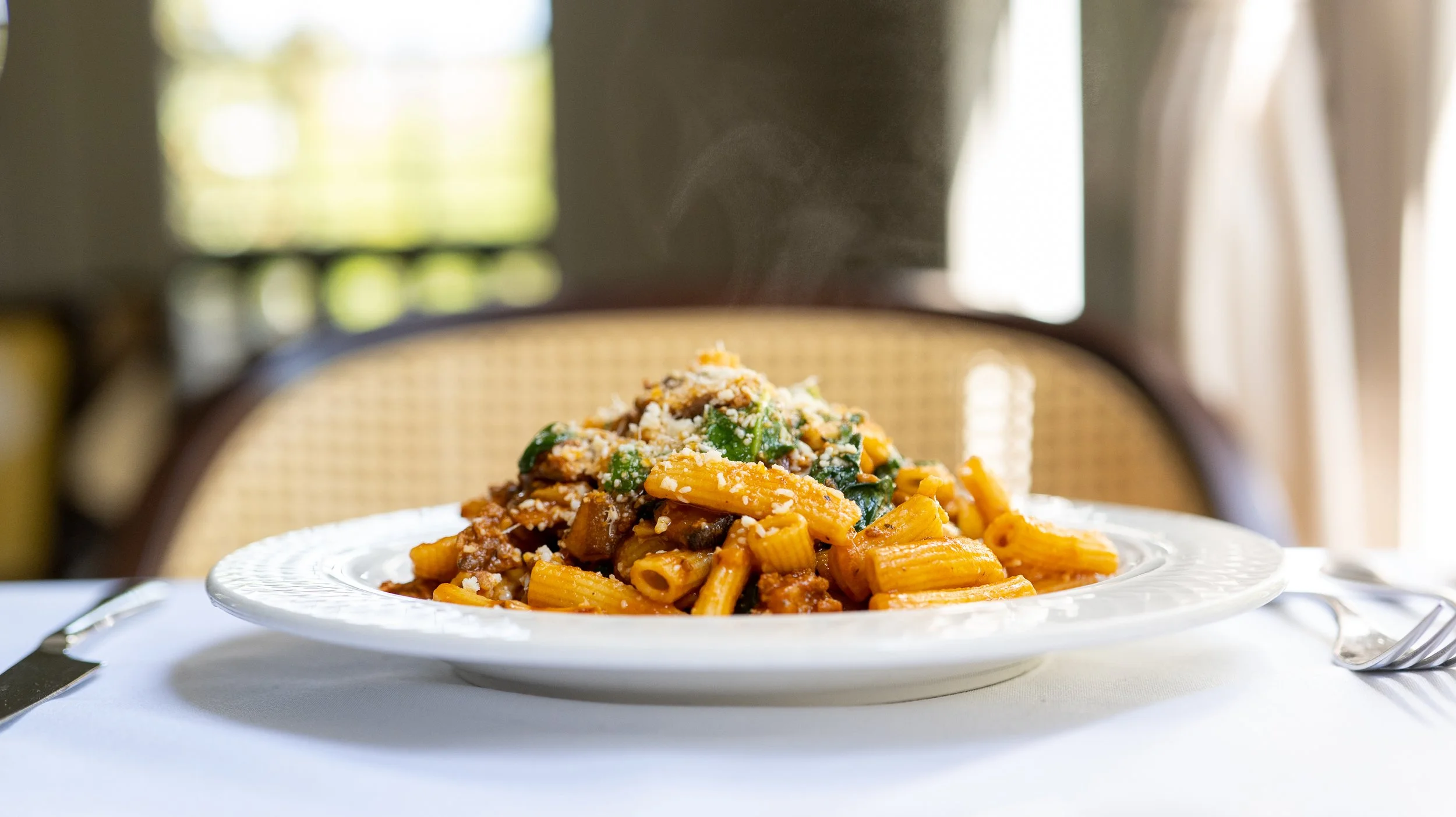 Close-up of a plate of cooked pasta with meat, vegetables, and cheese on a dining table.