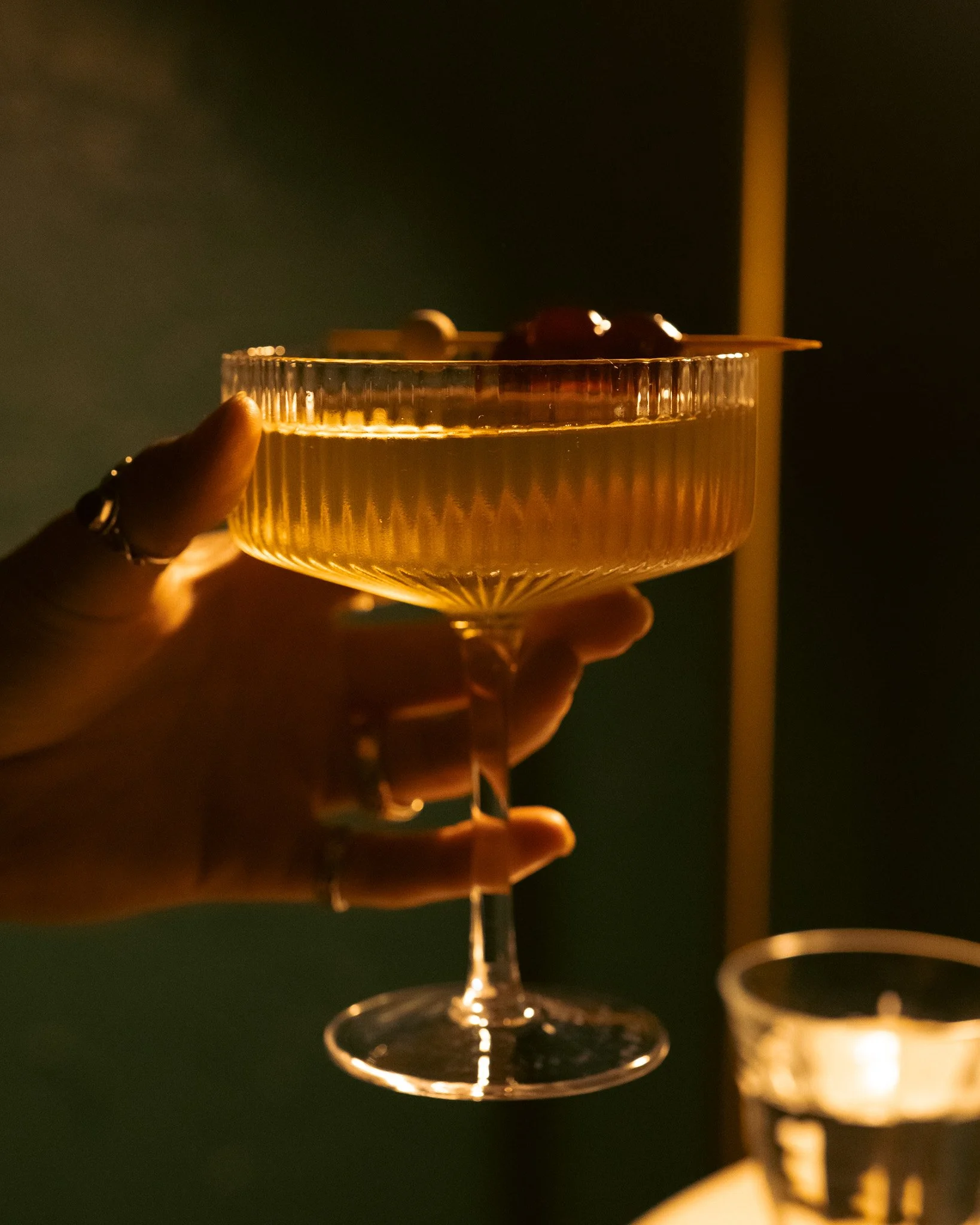 Close-up of a hand holding a glass of champagne or sparkling wine against a dark background, with some blurred light reflections.