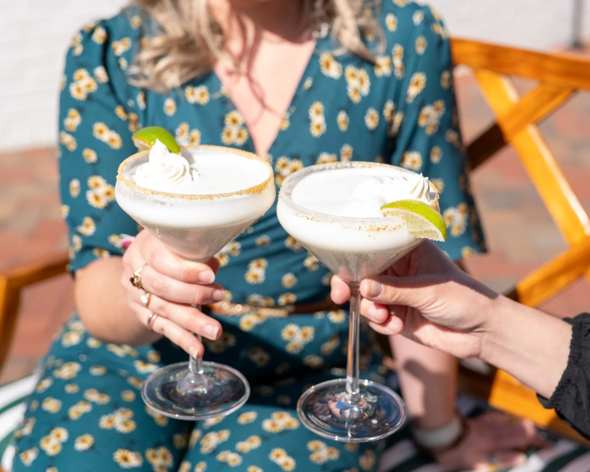 Two women holding margarita glasses with whipped cream and lime wedges during a celebration or gathering.
