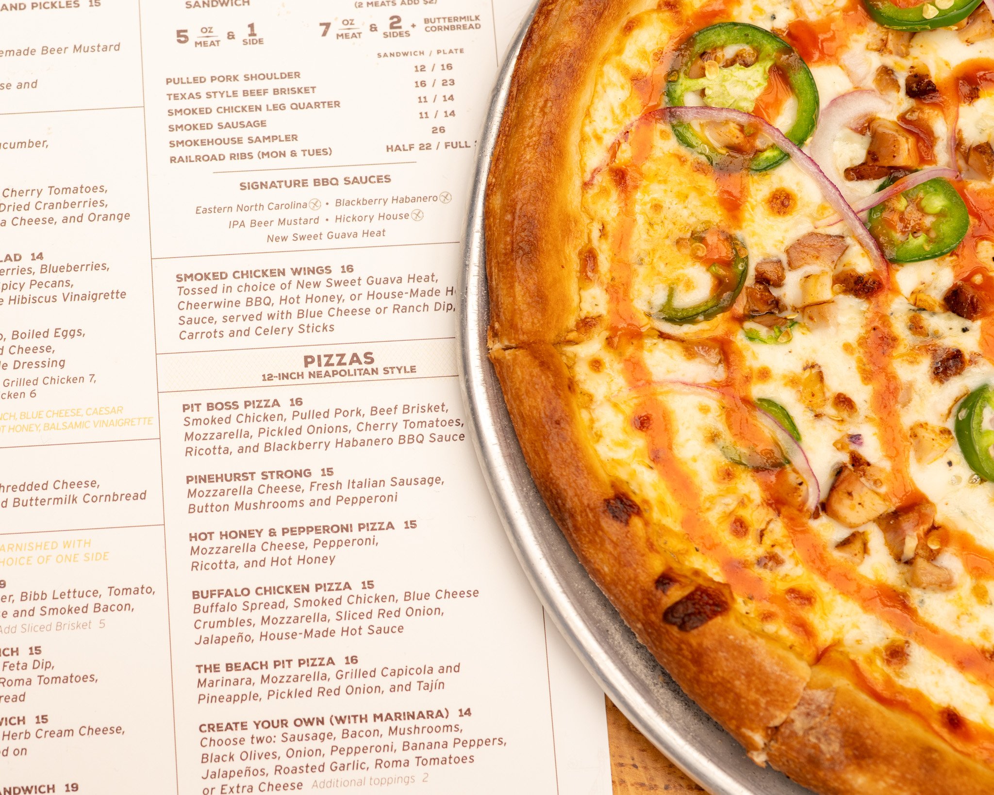 Close-up of a pizza with green peppers, onions, and cheese, partially visible on a metal tray, next to a menu listing various pizza options.