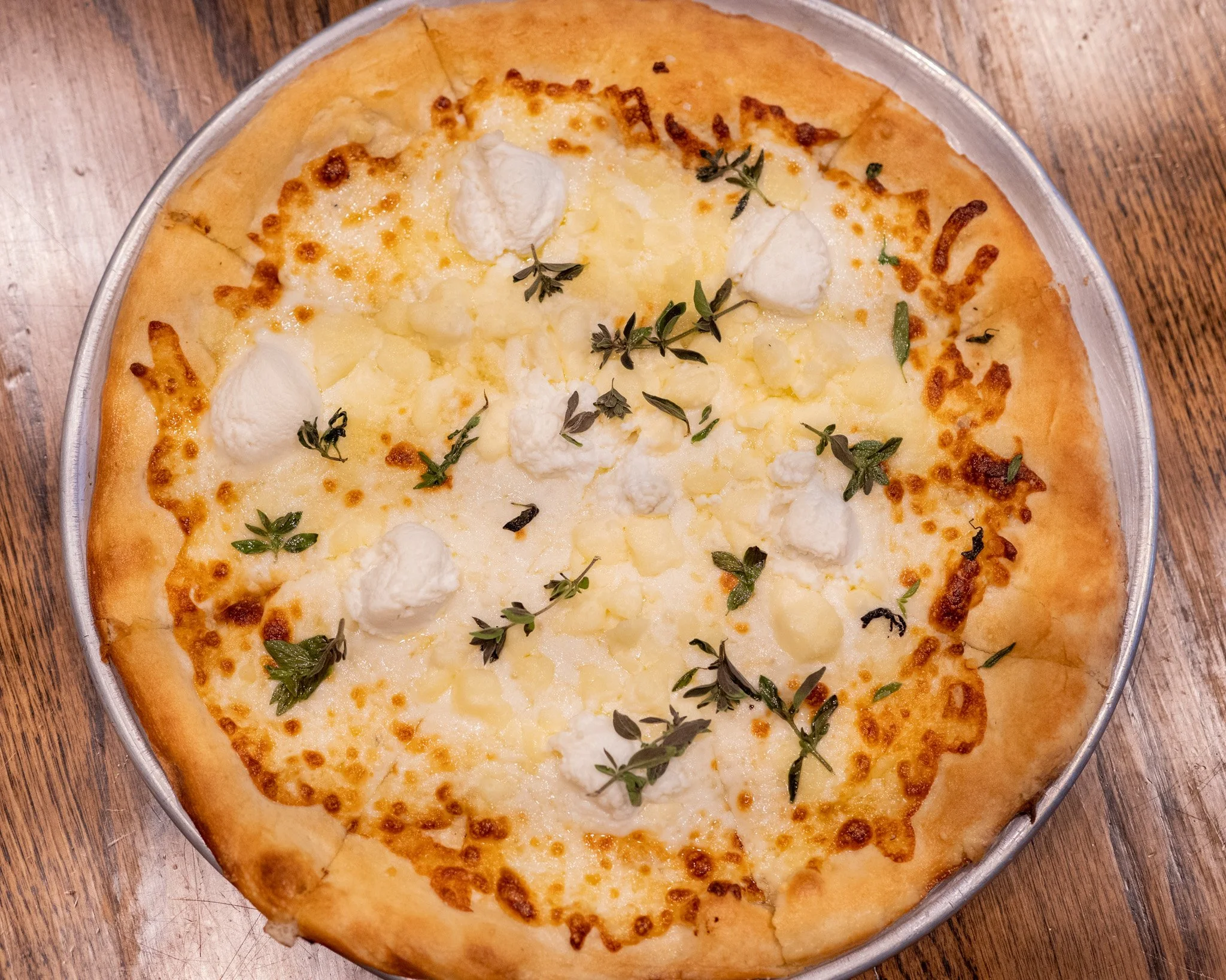 A cheese pizza topped with fresh herbs on a metal tray, placed on a wooden table.