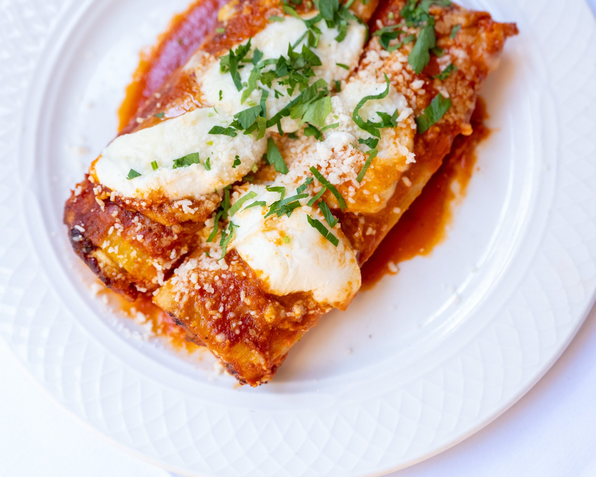 Close-up of a Mexican enchilada topped with sour cream, chopped cilantro, and grated cheese on a white plate.