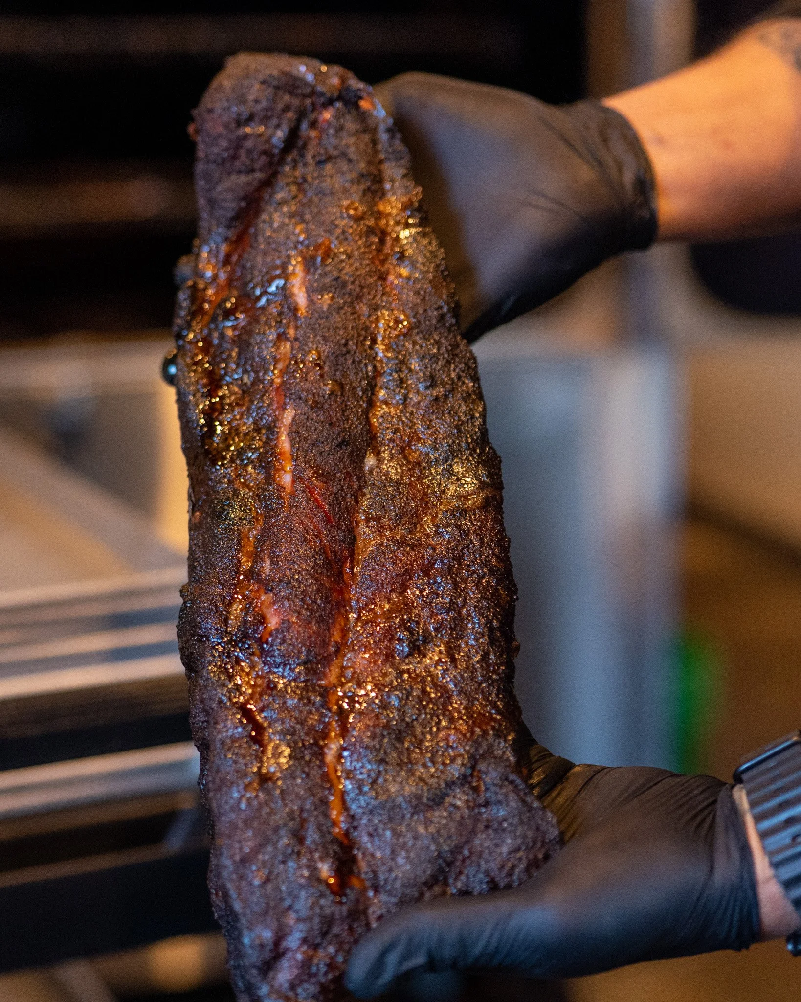 Close-up of a rack of ribs with a dark, spicy crust, glistening with sauce, held by a hand wearing a black glove.