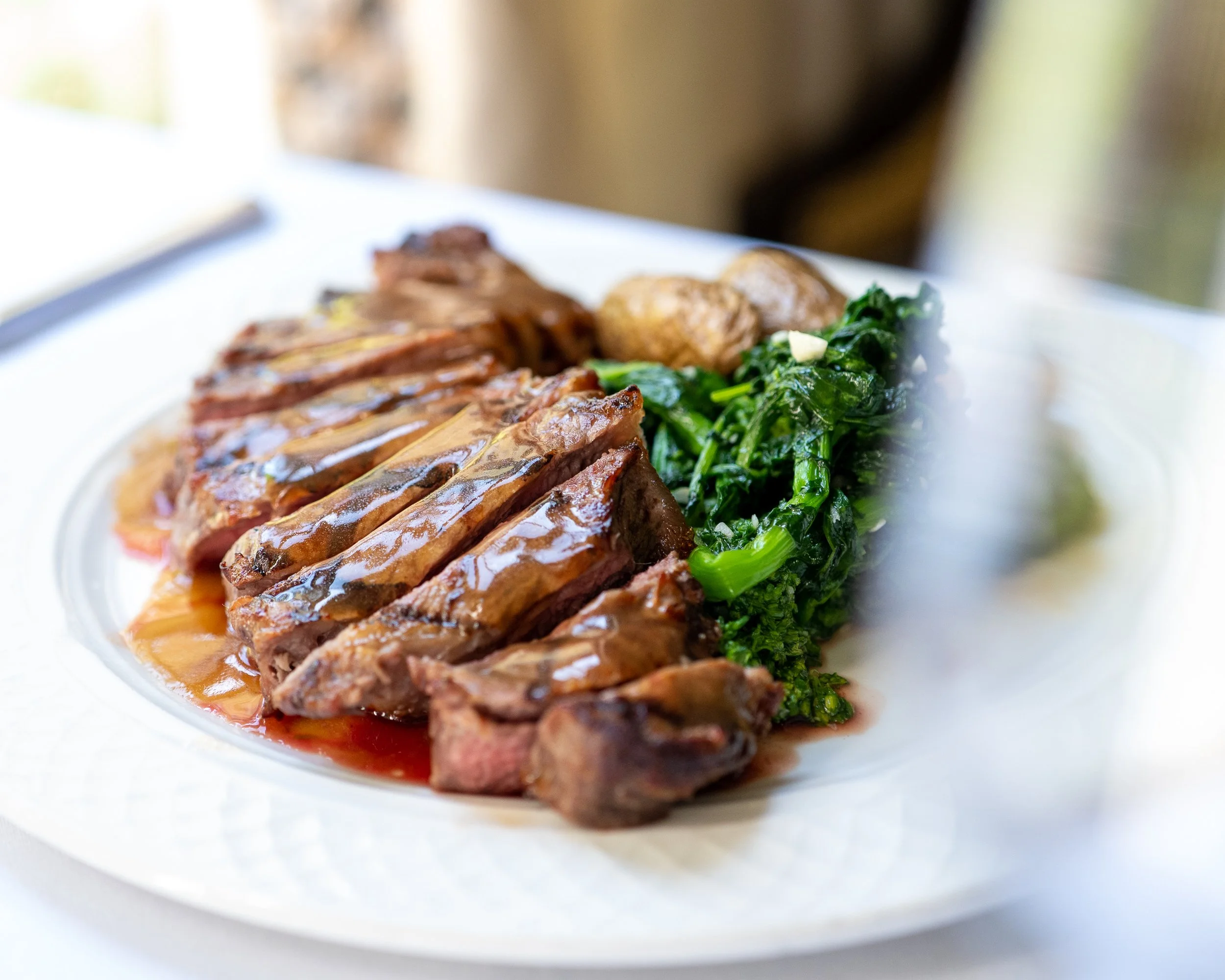 Slices of cooked meat, green leafy vegetables, and a side of potatoes on a white plate.