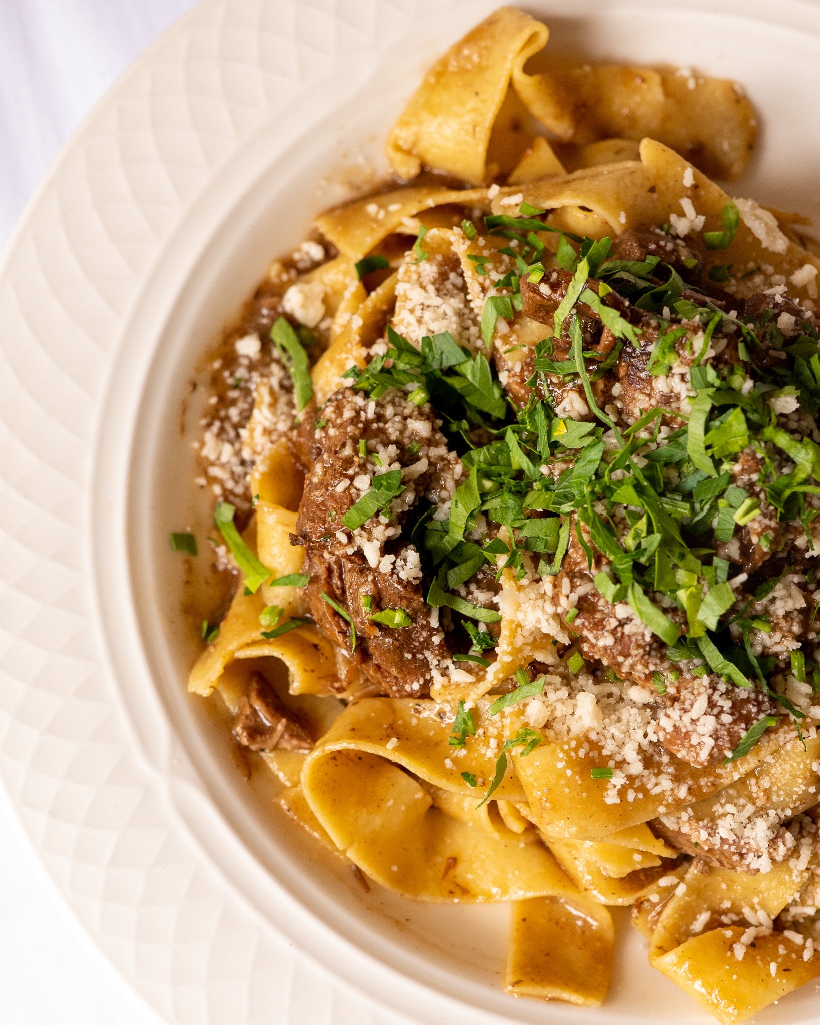 A plate of chef's pasta topped with chopped parsley and shredded cheese.