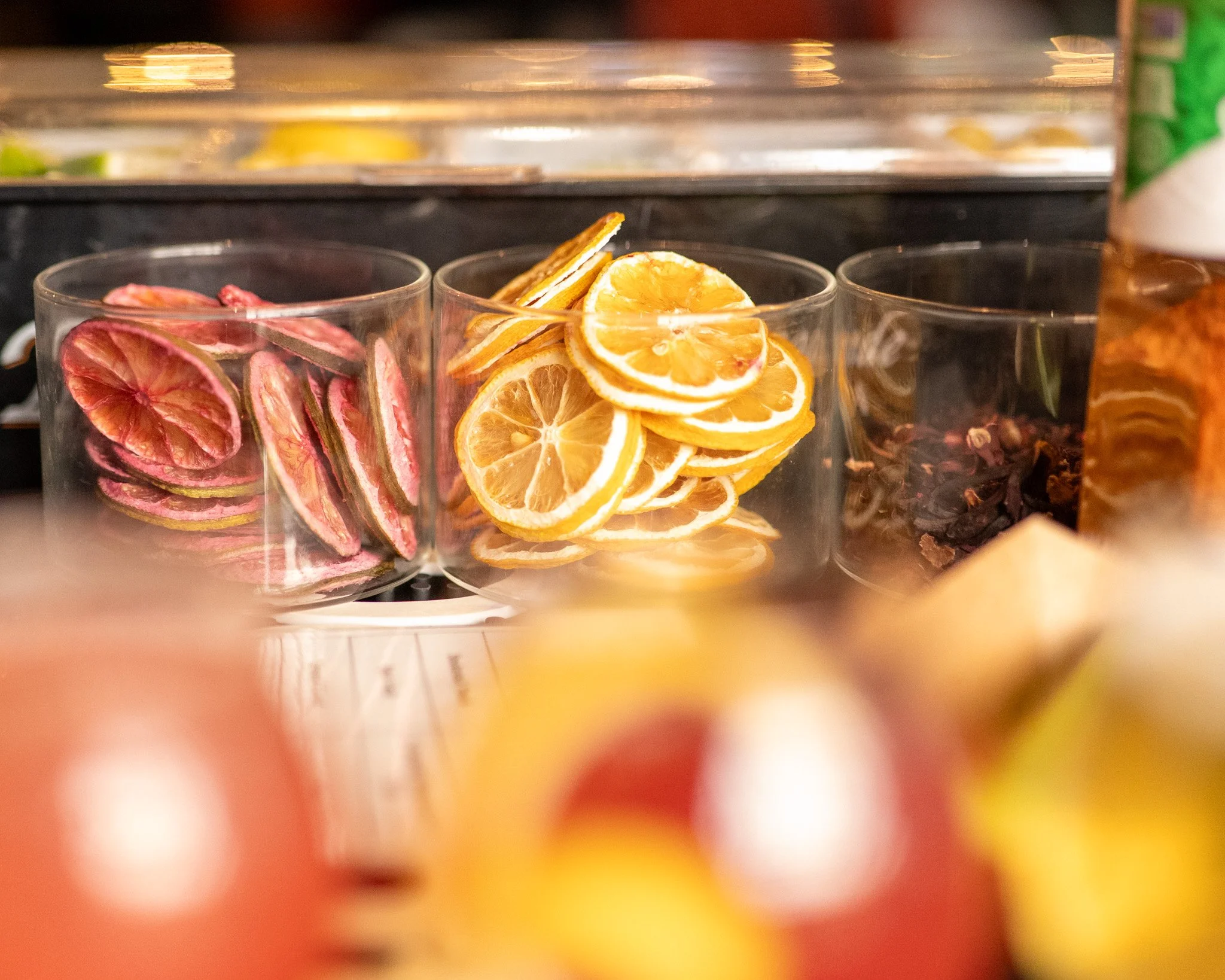 Three clear containers filled with dried fruit slices and herbs, including pink, orange, and yellow slices, on a shelf.