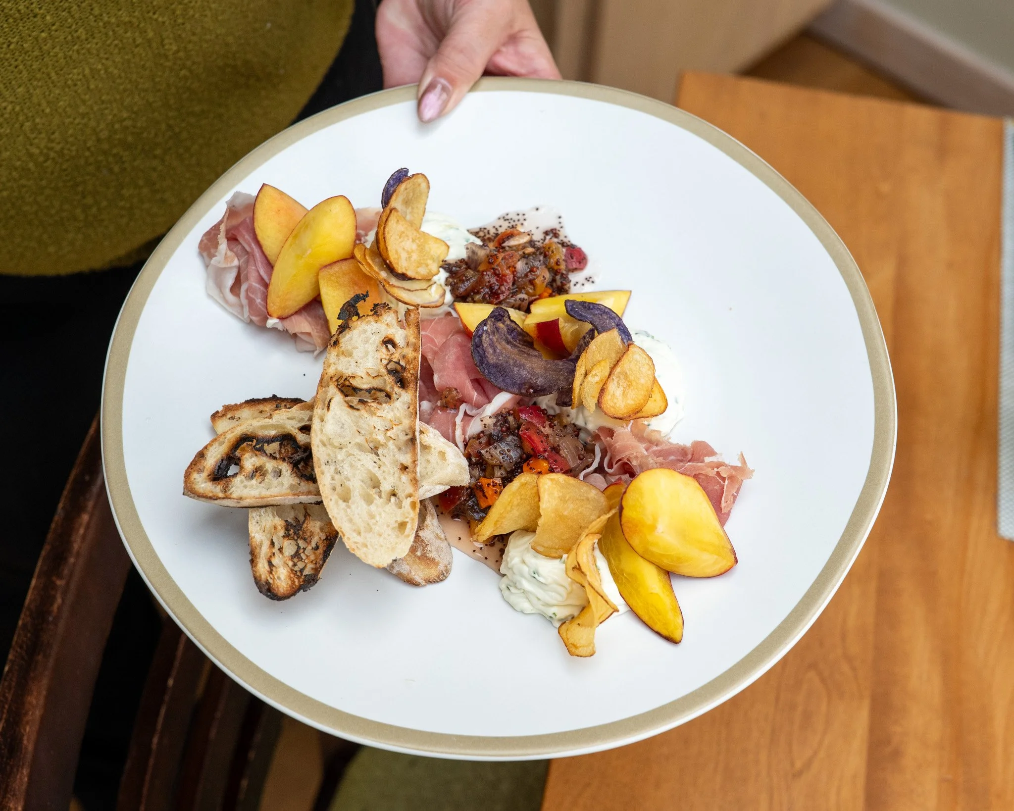 A plate of assorted appetizers, including slices of peaches, baguette slices, meat, and cheese, all arranged neatly for serving.