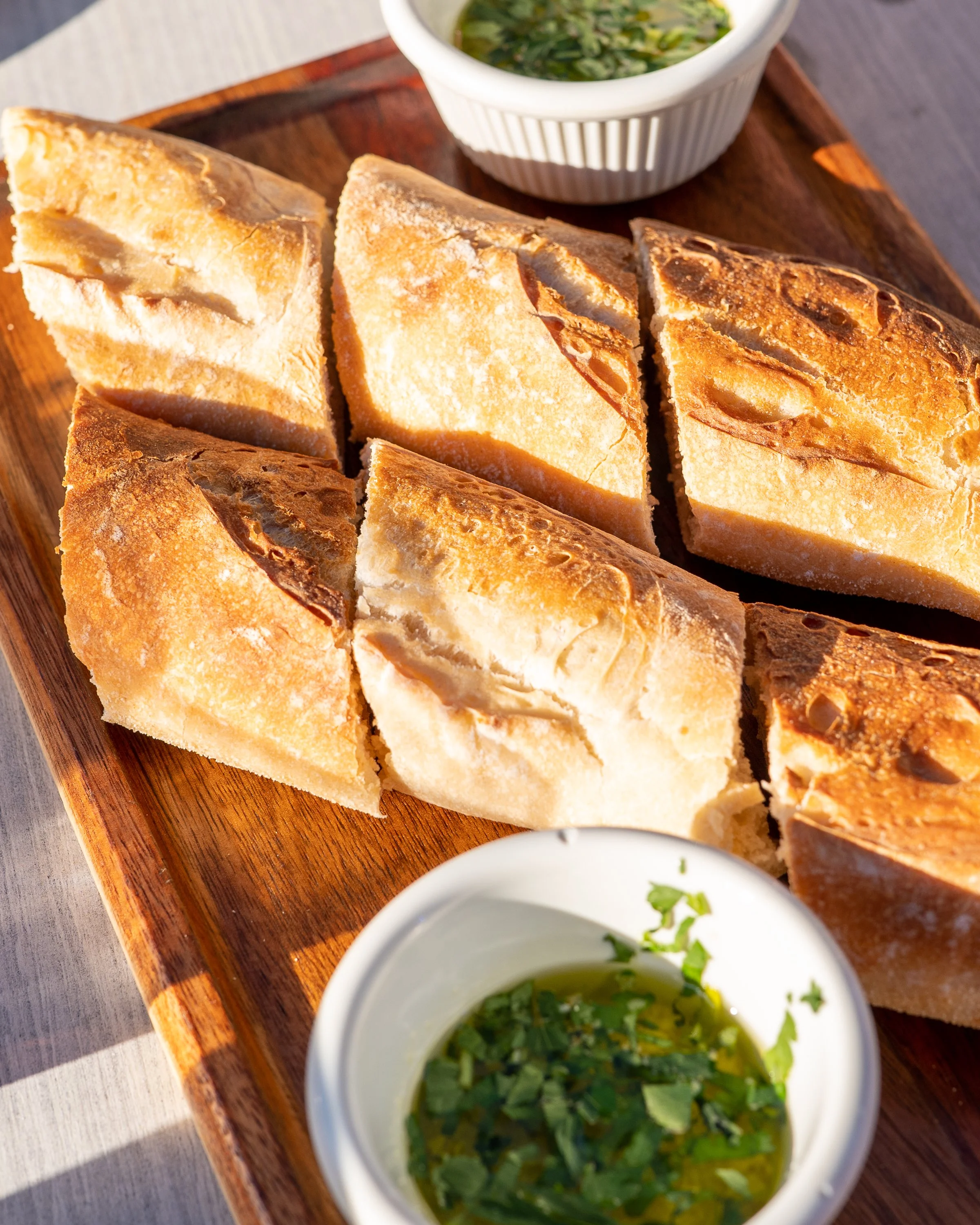 Slices of toasted bread on a wooden platter with a white bowl of green herb soup garnished with chopped herbs.