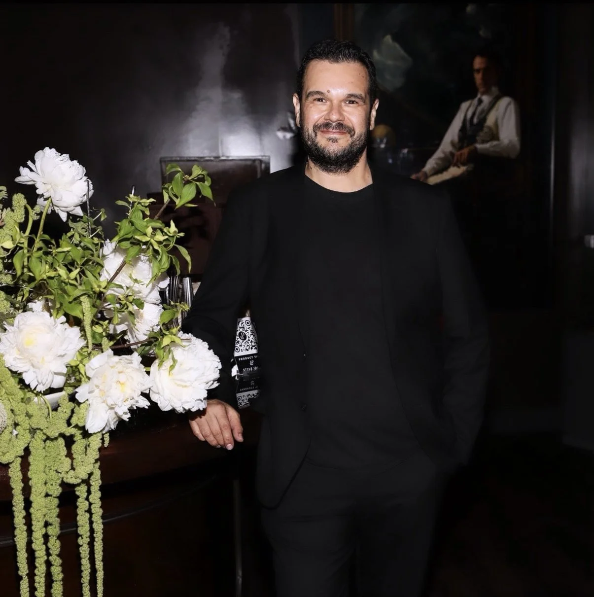 Portrait of Stevan Perea standing beside a floral arrangement at an indoor event.