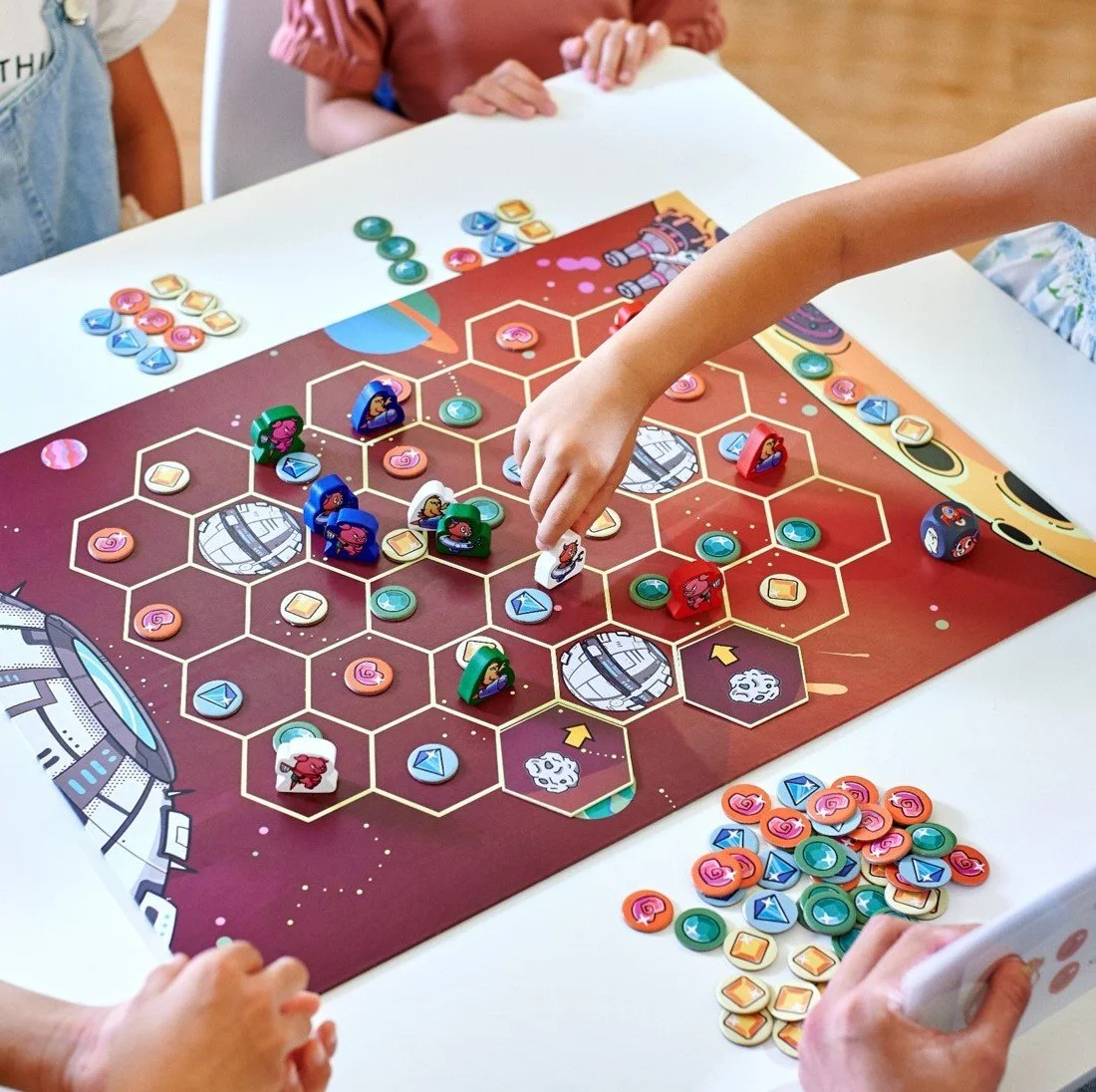 Children playing a space-themed board game with tokens and pieces on a hexagonal grid.