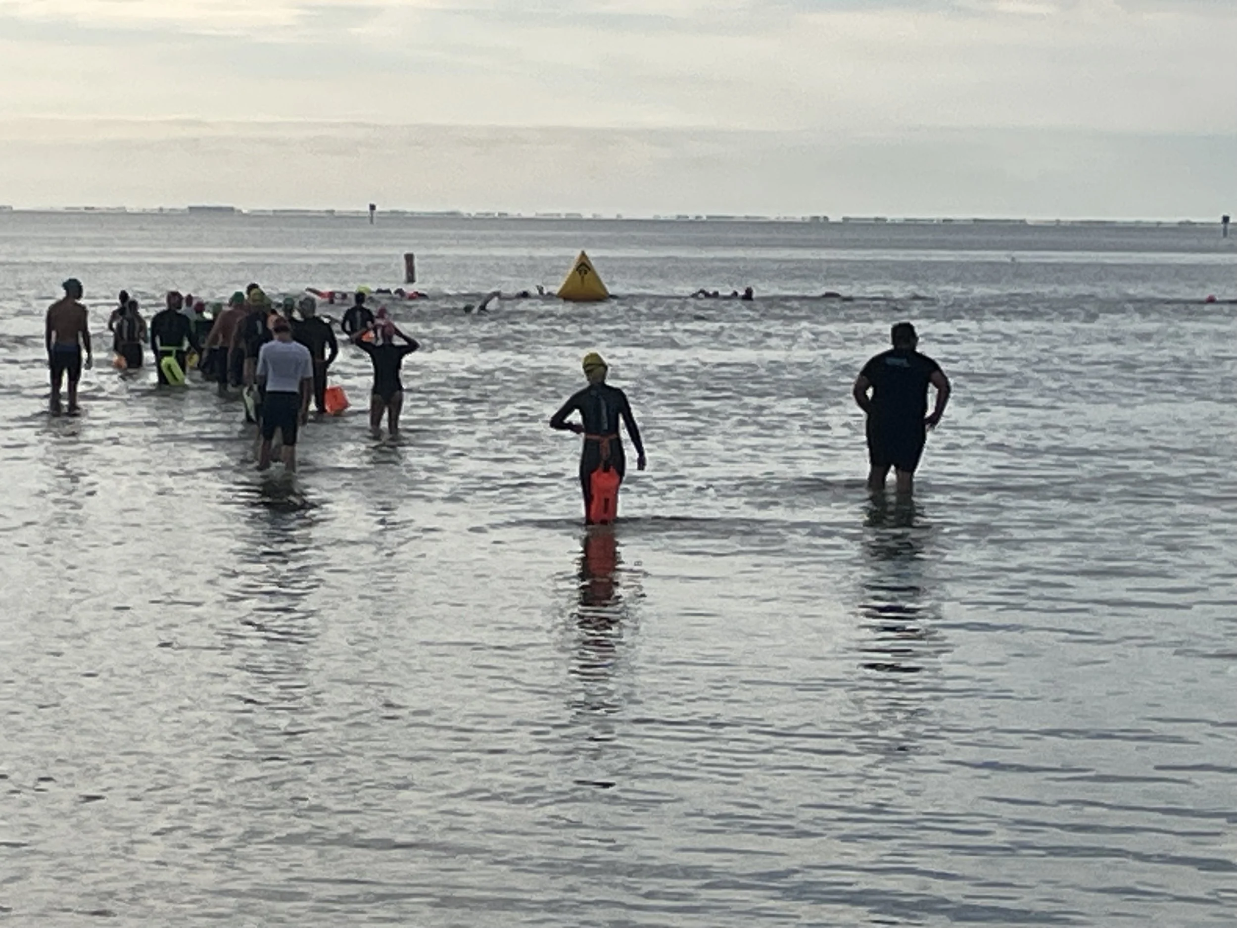 People practicing swimming and lifeguarding at the beach near a buoy, with calm water and cloudy sky in the background.