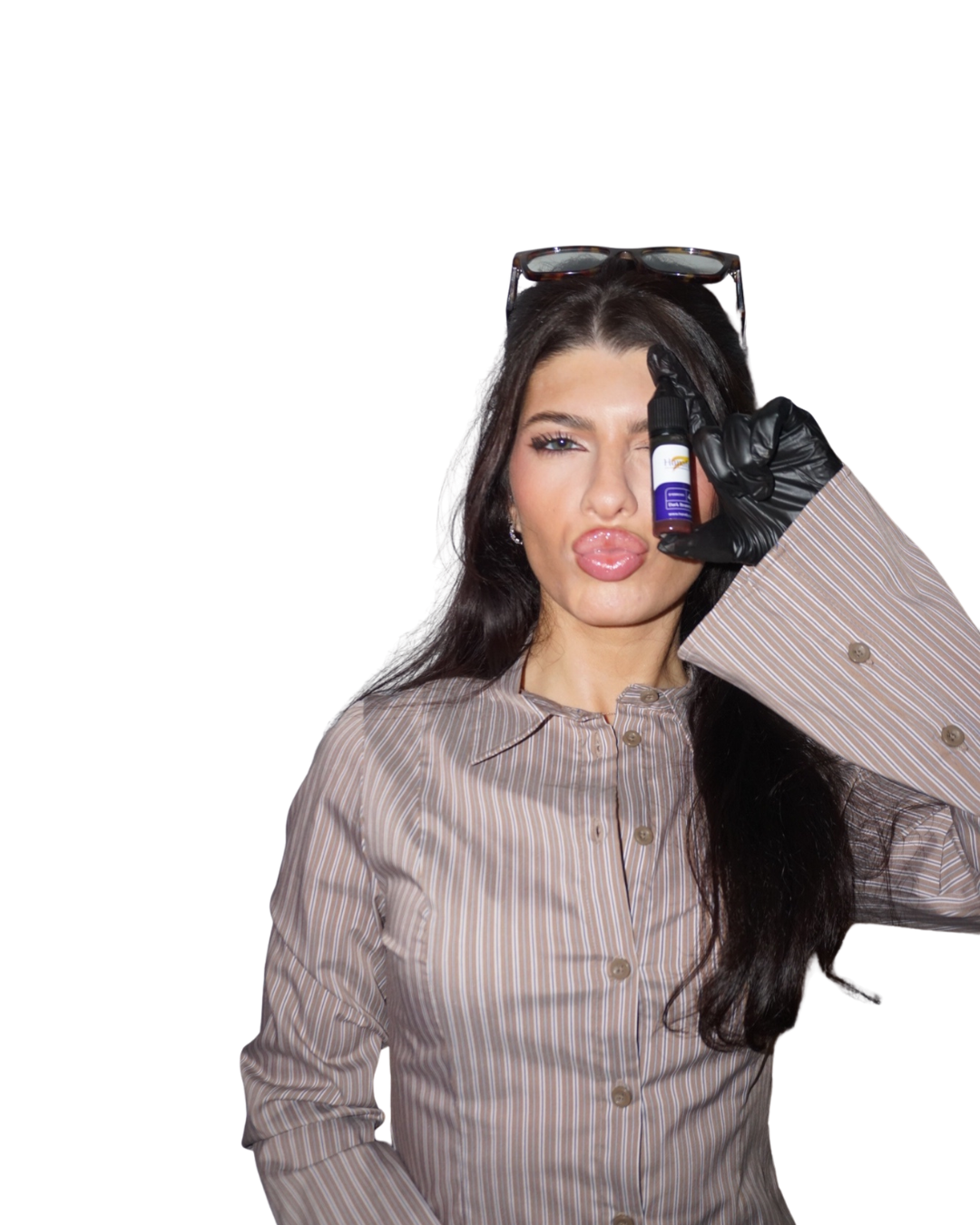 A woman with long dark hair and light skin winks and makes a silly face while holding a small bottle of eye drops near her eye. She is wearing a striped button-up shirt, black gloves, and sunglasses resting on her head.