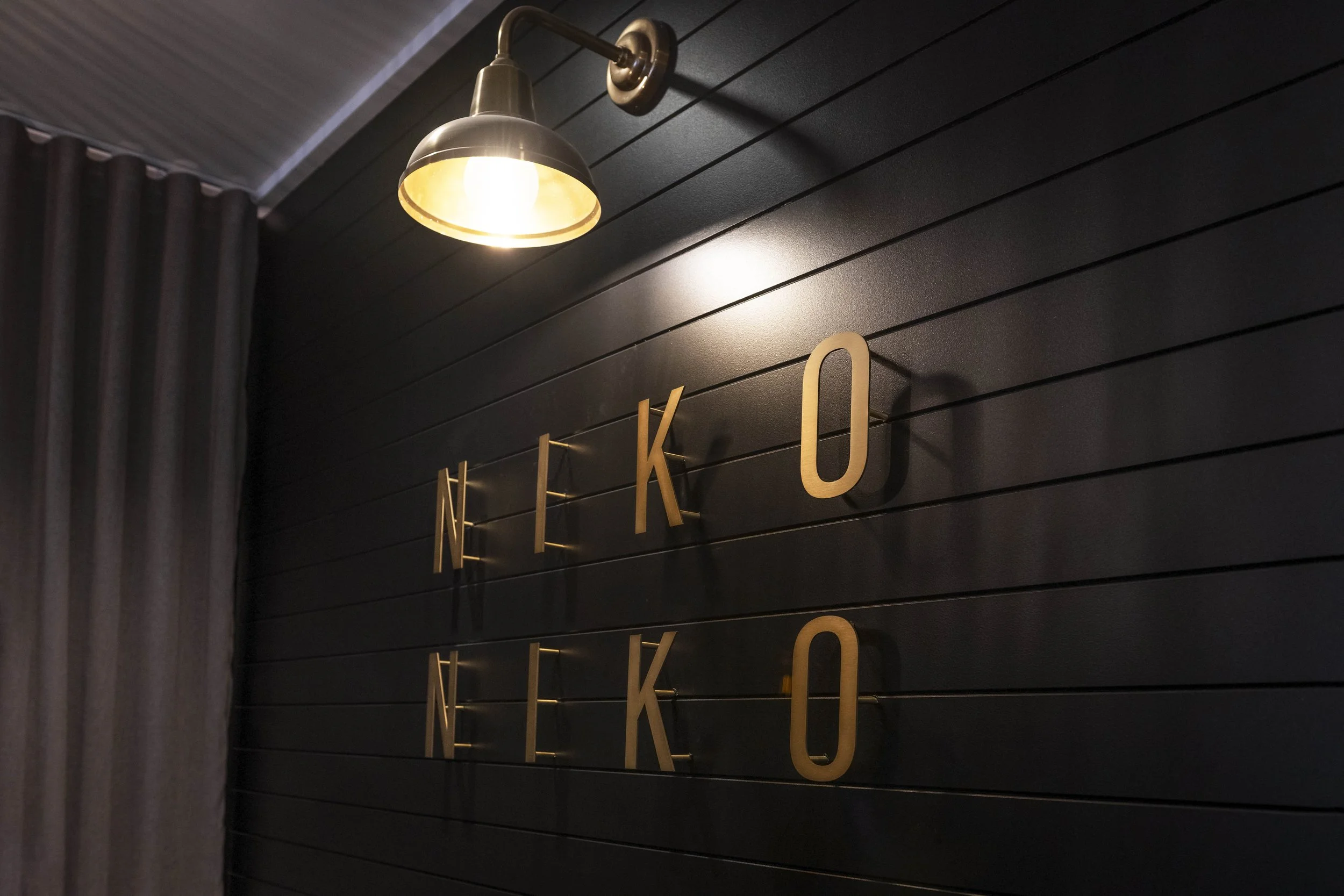 Close-up of a wall with metallic letters spelling 'NOK' and a wall-mounted lamp illuminating the wall.
