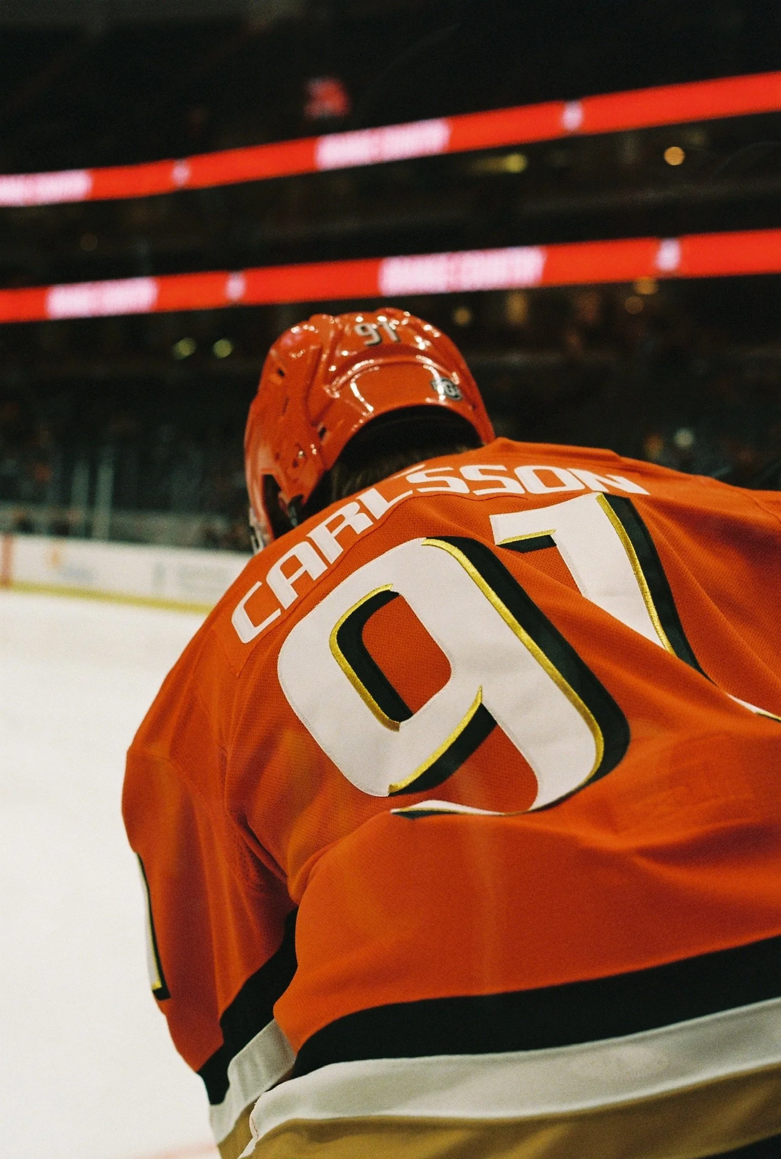 Close-up of an ice hockey player wearing an orange jersey and helmet, number 91, on the ice rink.