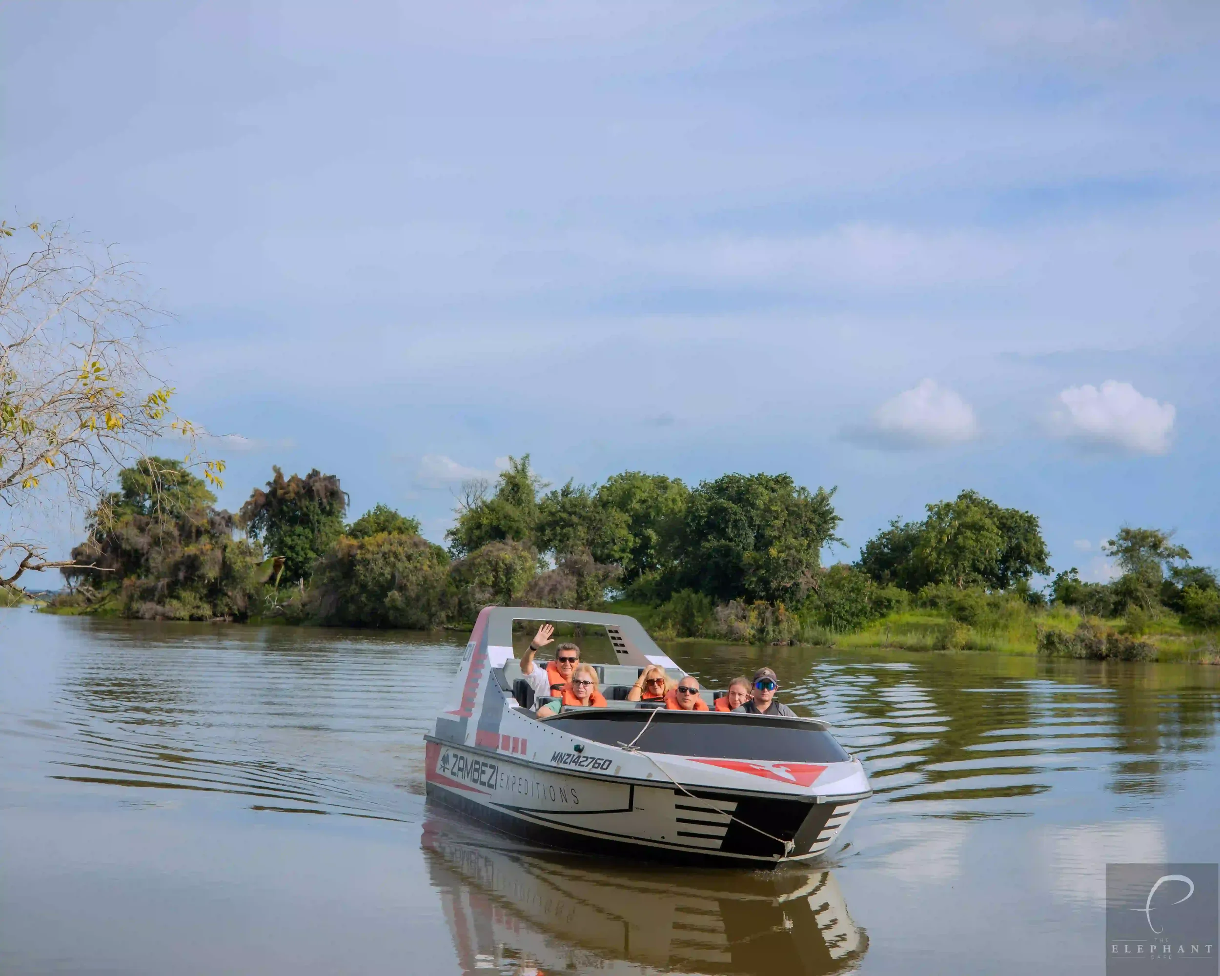 A group of seven people enjoying a boat ride on a calm river, surrounded by trees and a partly cloudy sky.