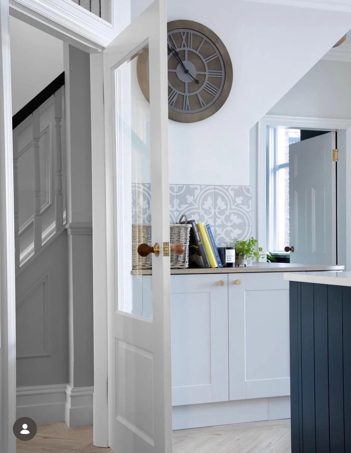 Interior of a modern kitchen with white cabinetry, a dark blue island, decorative tiles, and a large wall clock showing 6:58.
