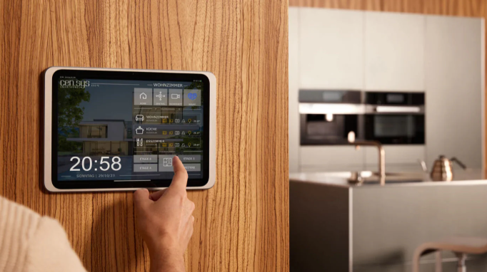 Person using a smart home control tablet on a wooden wall in a modern kitchen.