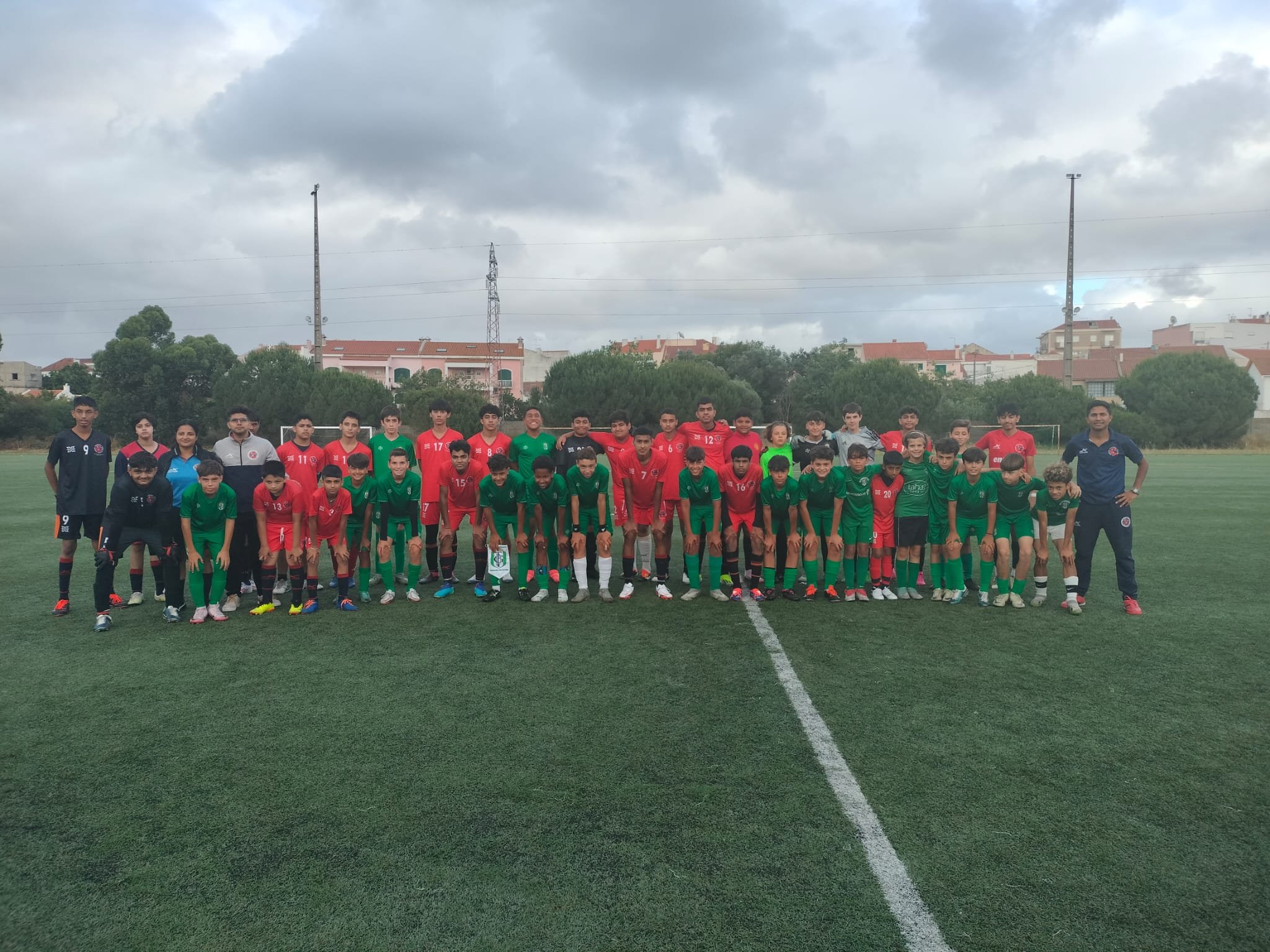 Group of young soccer players and coaches posing for a team photo on a soccer field on a cloudy day.