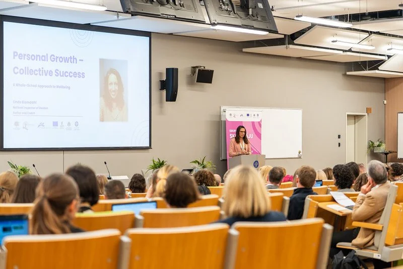 A woman giving a presentation in a large conference room filled with seated attendees, slide titled 'Personal Growth - Collective Success' is projected on the screen.