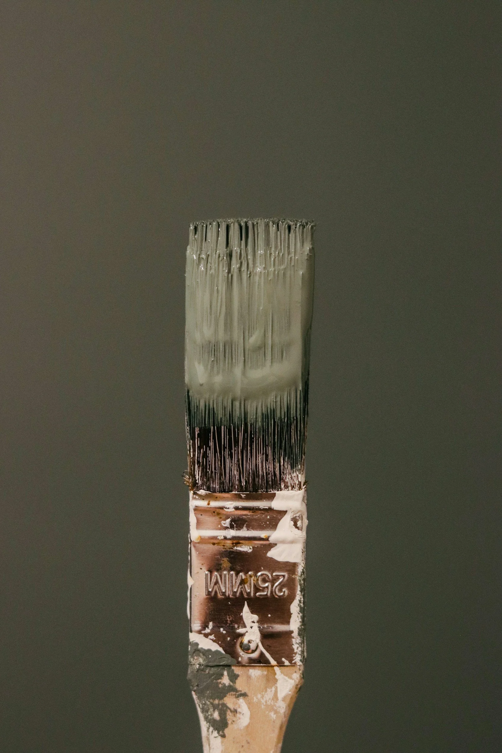 Close-up of a paintbrush with traces of white and brown paint on the metal ferrule and handle, set against a dark background.