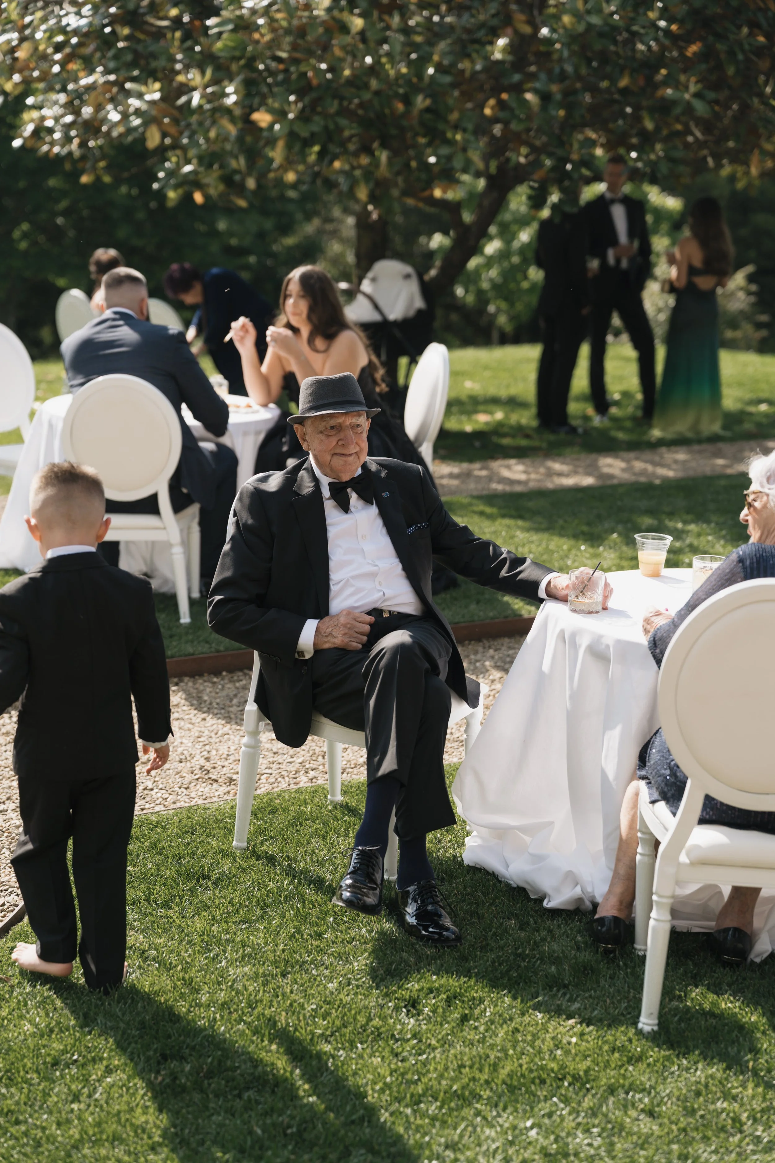 People at a formal outdoor event, with some seated at tables and others standing and talking in the background.