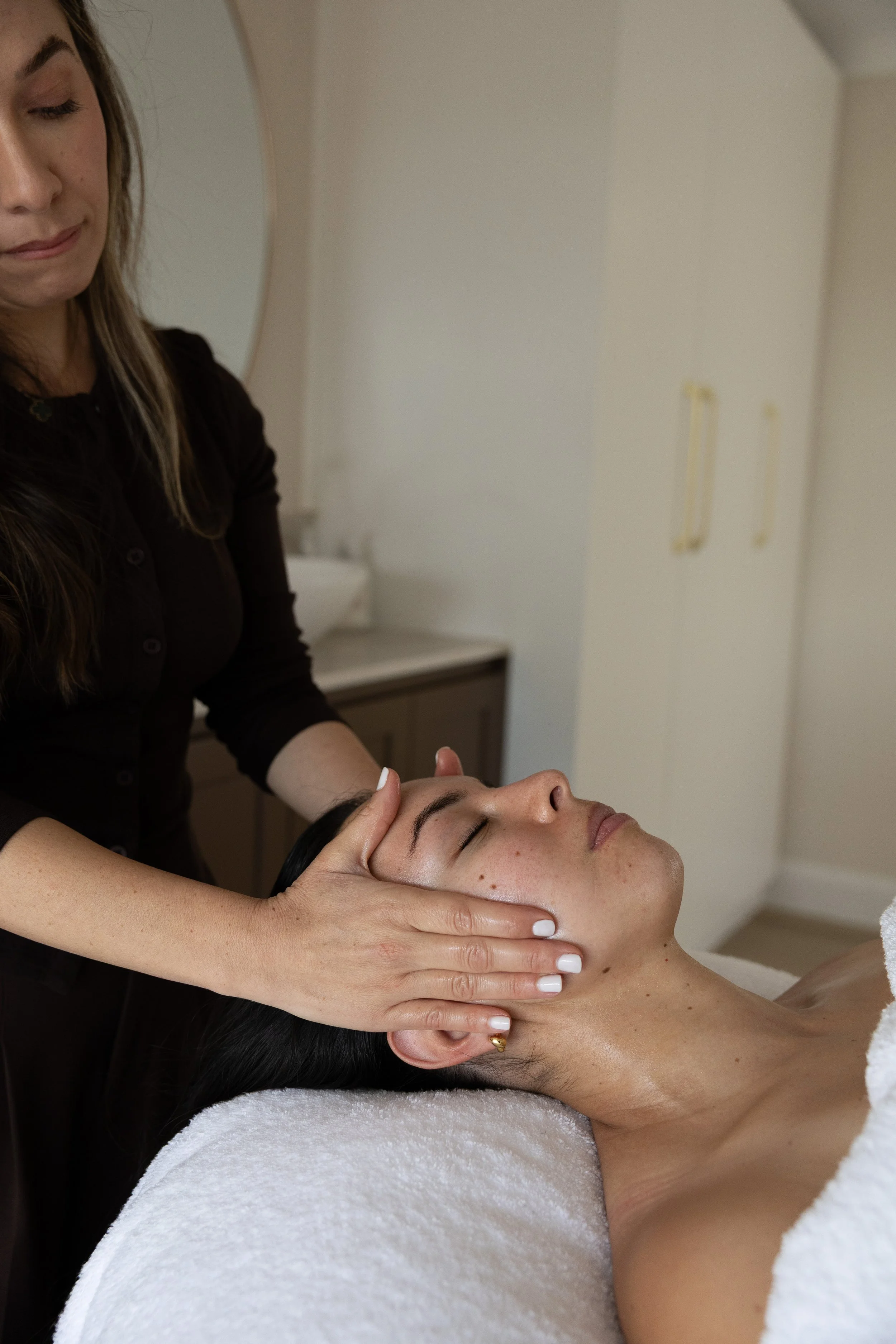 A woman receiving a facial massage or treatment from a therapist in a spa or clinic setting.