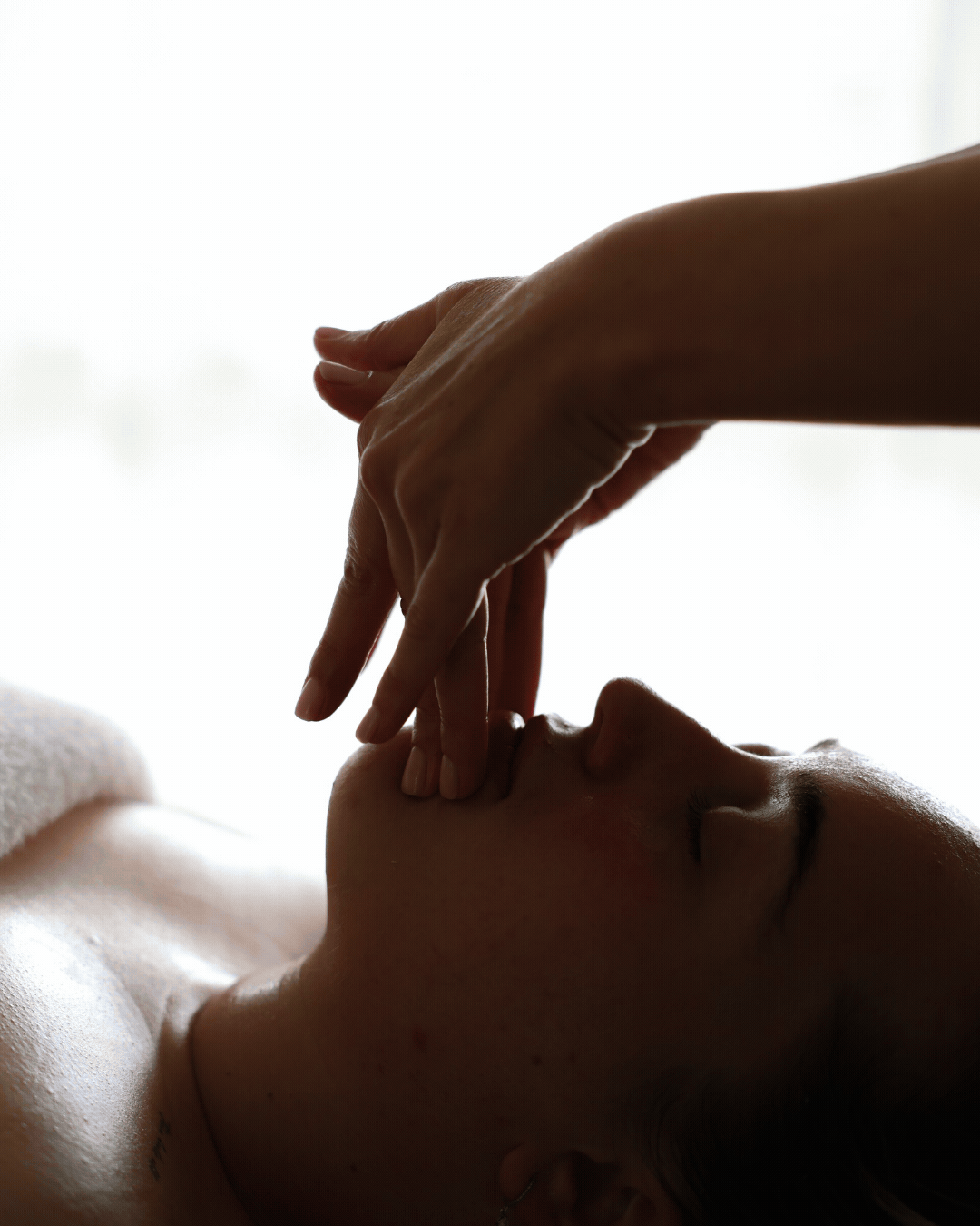 A person receiving a facial massage or skincare treatment, lying down with eyes closed, with hands gently touching the face.
