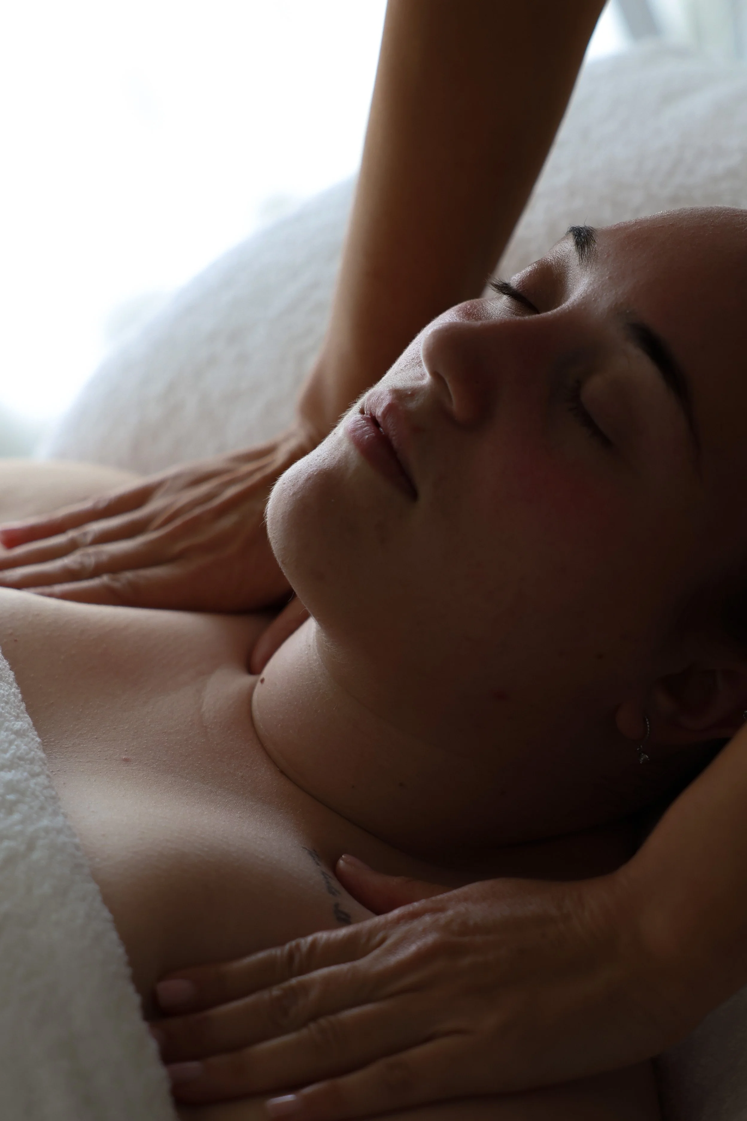 A person lying down with eyes closed, resting or relaxing, with hands gently placed on their chest, in a calm and peaceful setting.